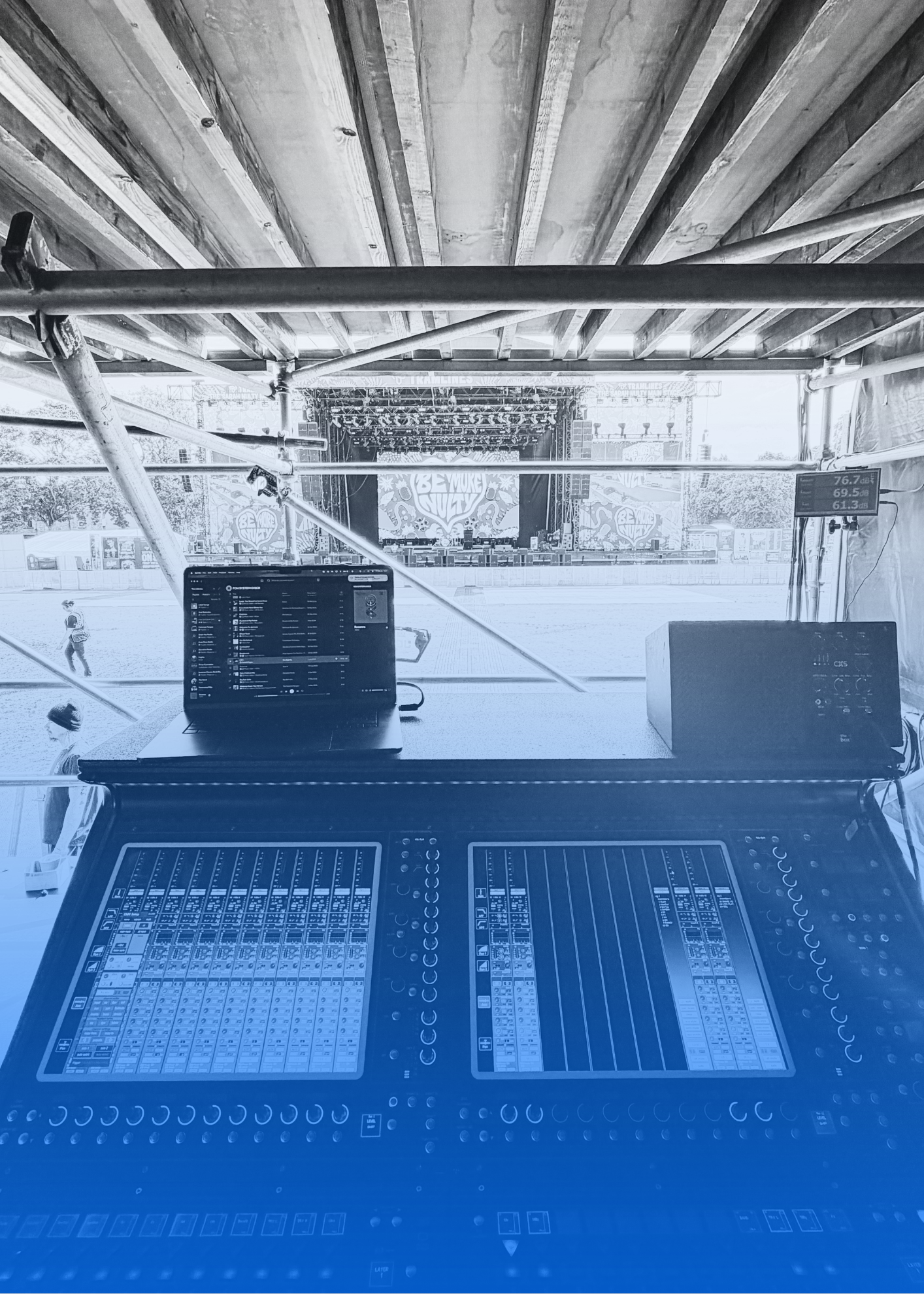 An outdoor stage at a music festival with a large backdrop featuring the text 'Be More Sub' and artwork, surrounded by trees and festival infrastructure, as seen through a ventilation opening.