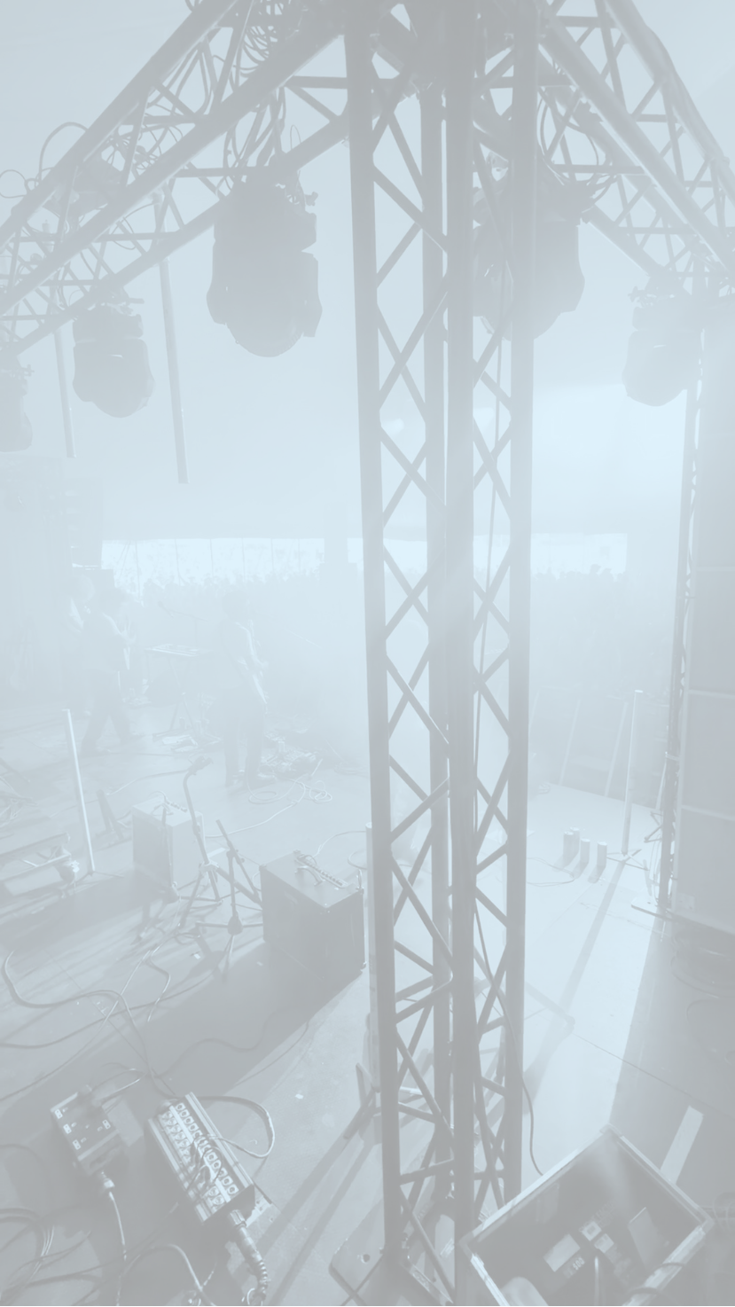 Stage setup with metal truss structure, lighting fixtures, and audio equipment on a foggy or hazy atmosphere.