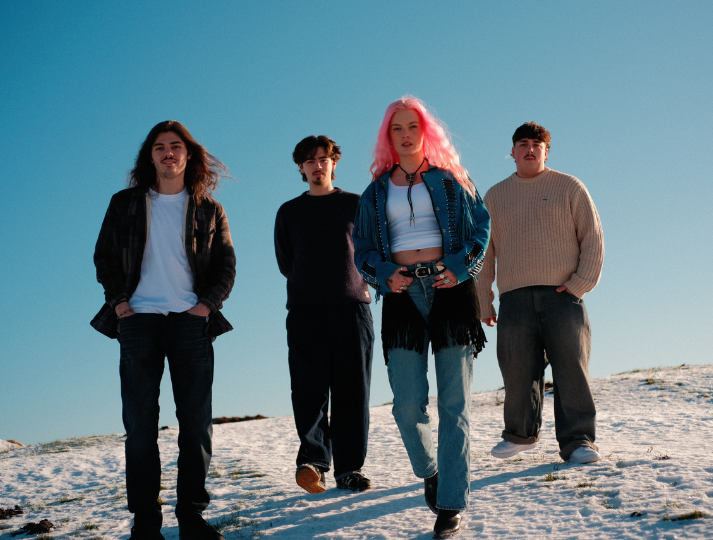 Four young adults walking outdoors on a snowy hill on a clear day.