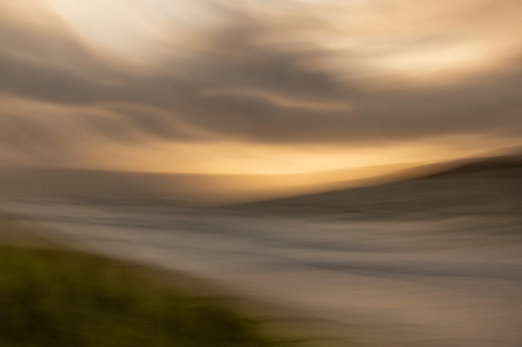 Abstract image of a cloudy sky with sunset looking over a beach to a hill in the background.