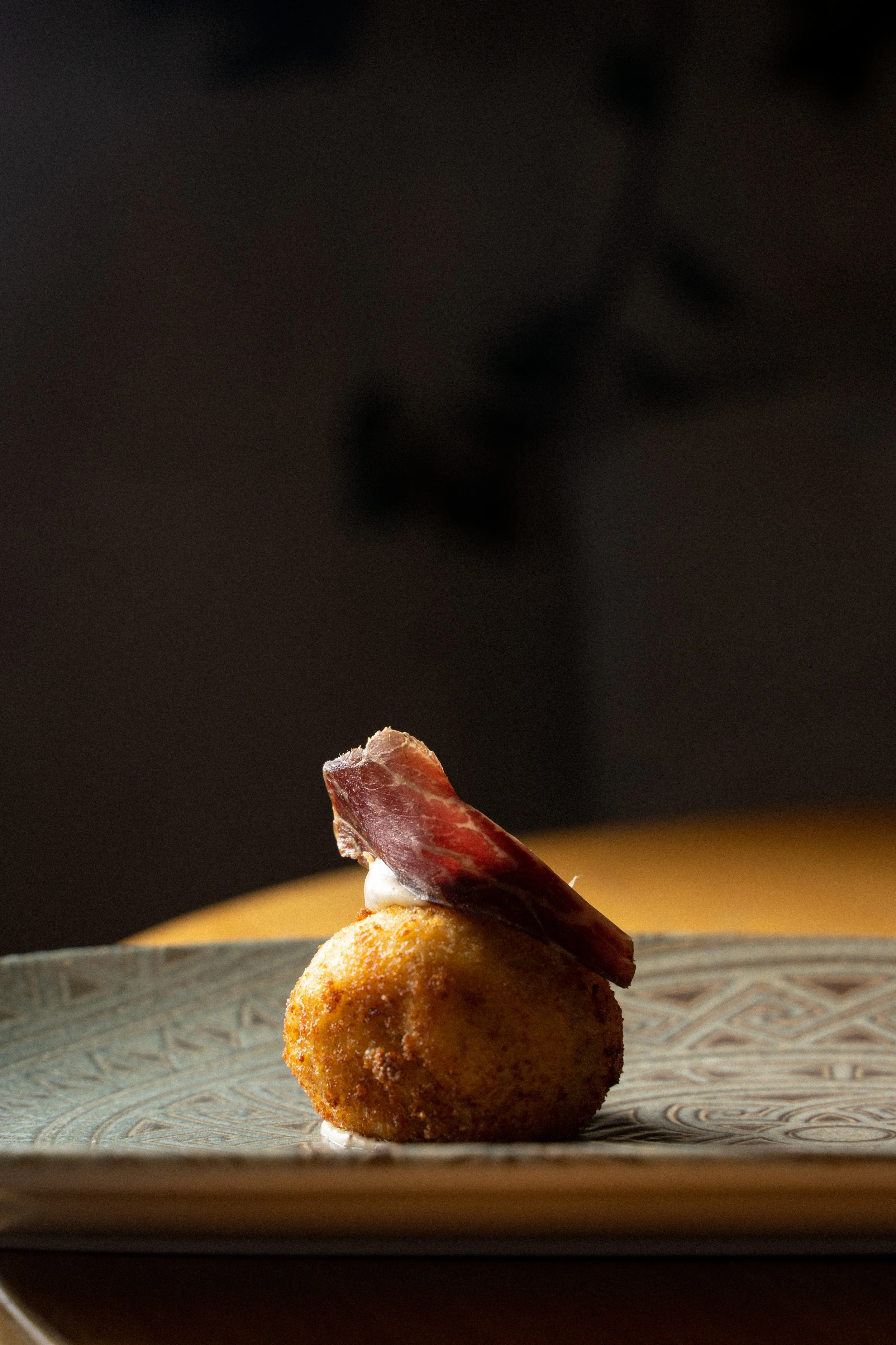 Bola de arroz empanizada con tocino encima, sobre un plato decorativo.