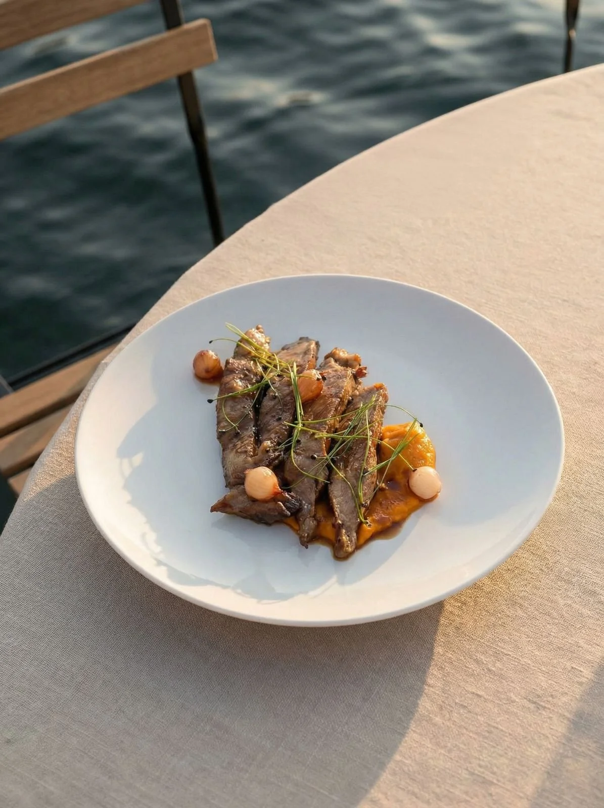 Plato de pescado con vegetales y nueces en una mesa junto al agua.