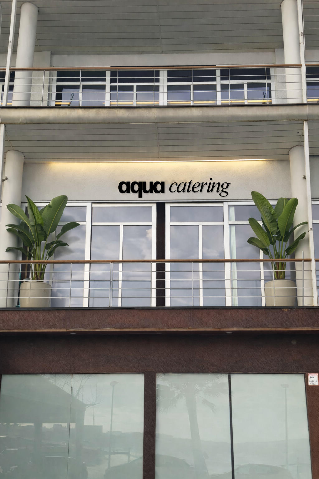 Fachada de un edificio con un letrero que dice 'agua catering', plantas en macetas y balcones con barandales de metal.