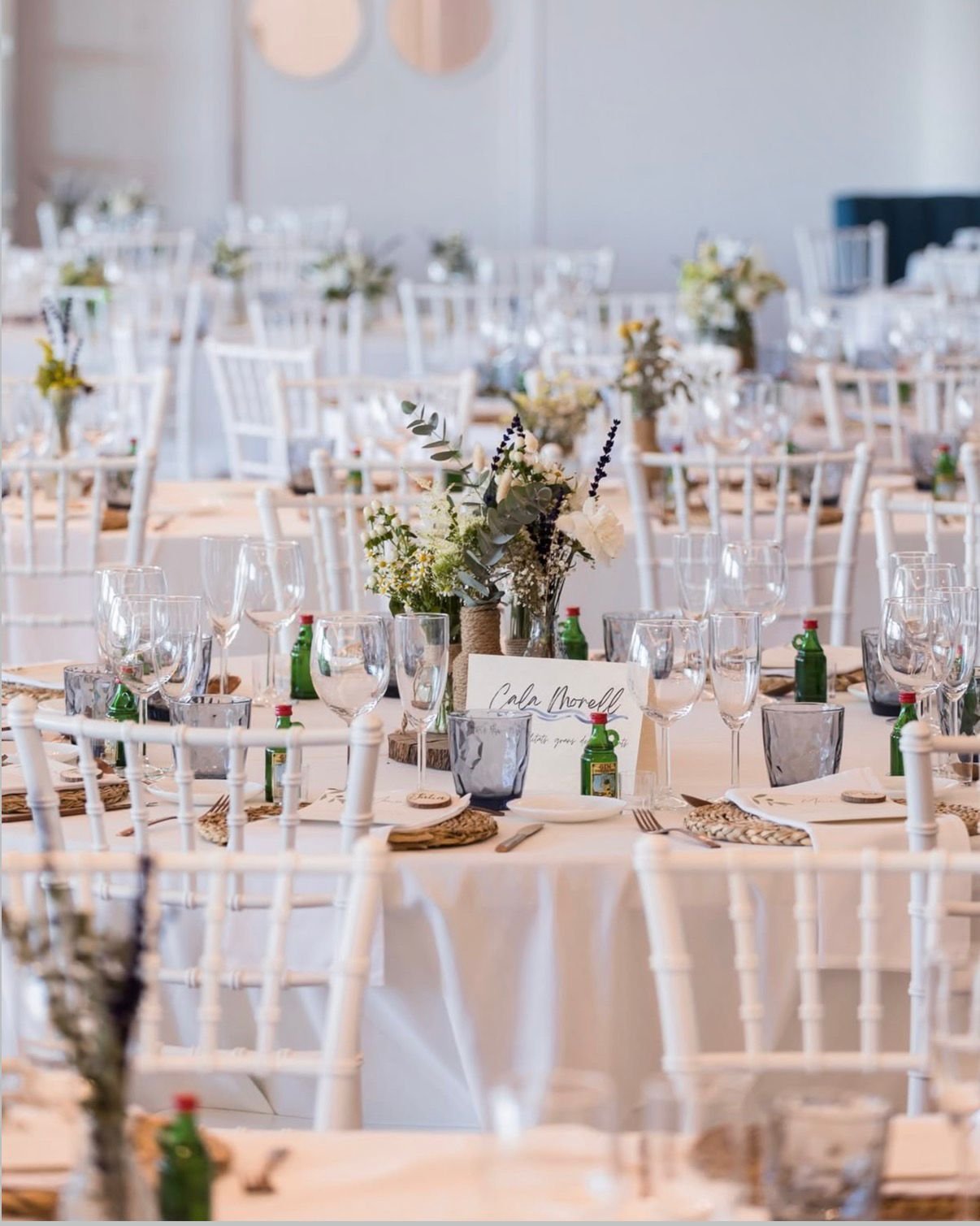 Mesas decoradas con copas, platos, cubiertos y centros de flores en una celebración o evento.