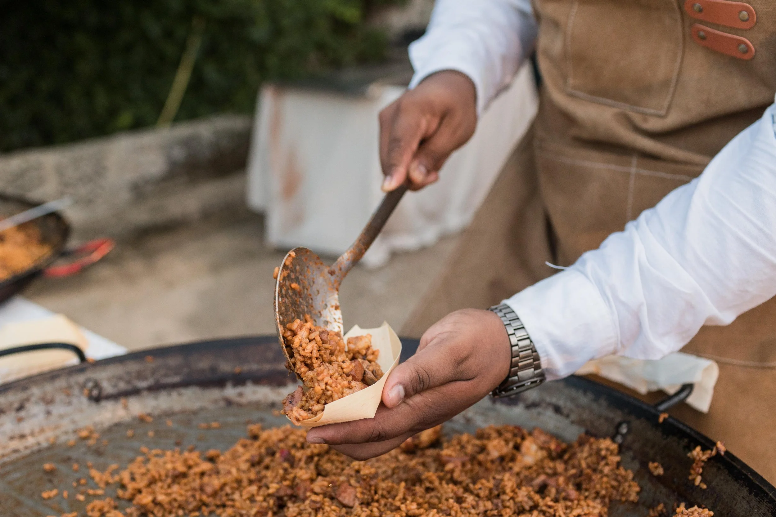 Persona sirviendo un plato de comida en un puesto de comida callejera con una cuchara grande y una sartén con arroz y carne en el fondo.