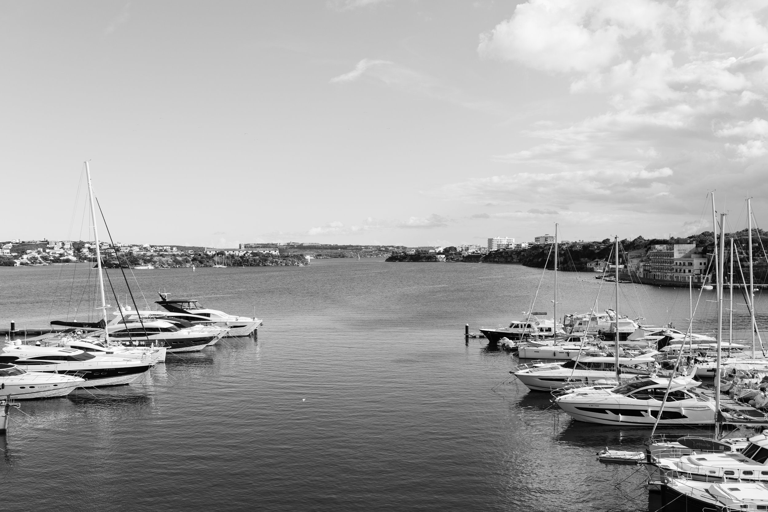 Embarcaciones de lujo amarradas en un muelle en una bahía con edificios en el fondo, bajo un cielo con nubes.