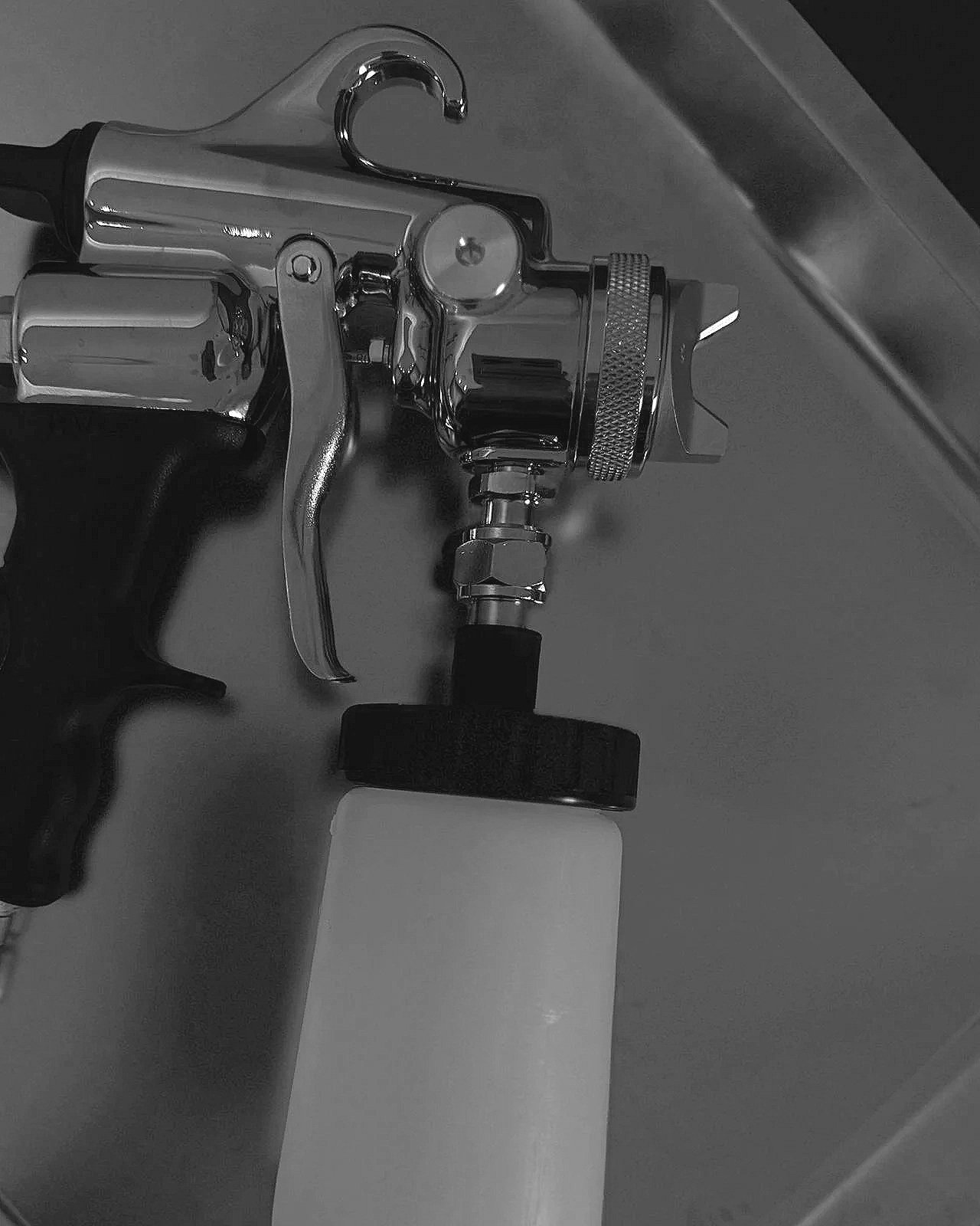 Ein Farbspritzpistole mit Pistolengriff, Düse und Druckregler, die an einem weißen Behälter befestigt ist.