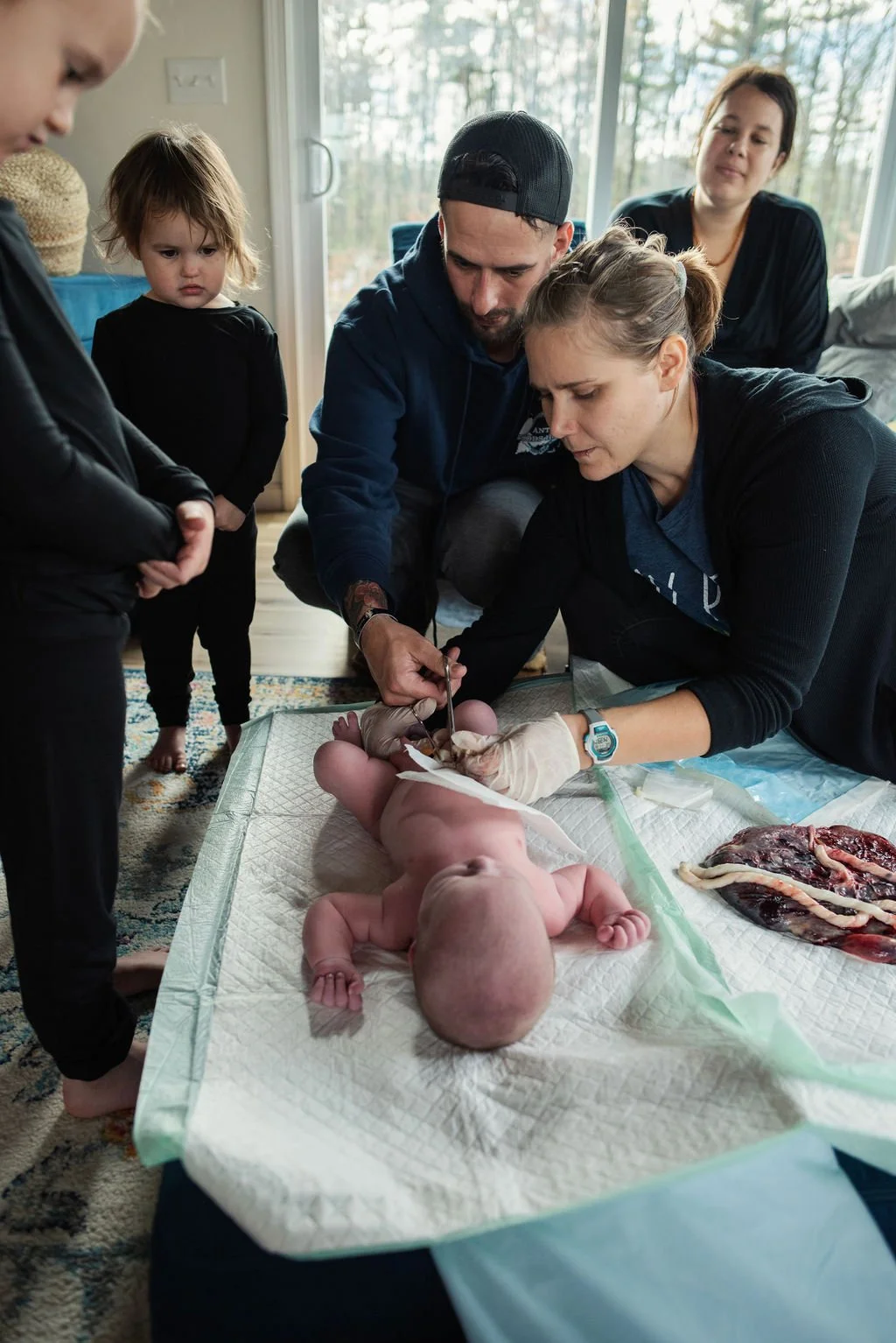 Midwife Sarah Mead performing a newborn exam and helping dad cut the cord