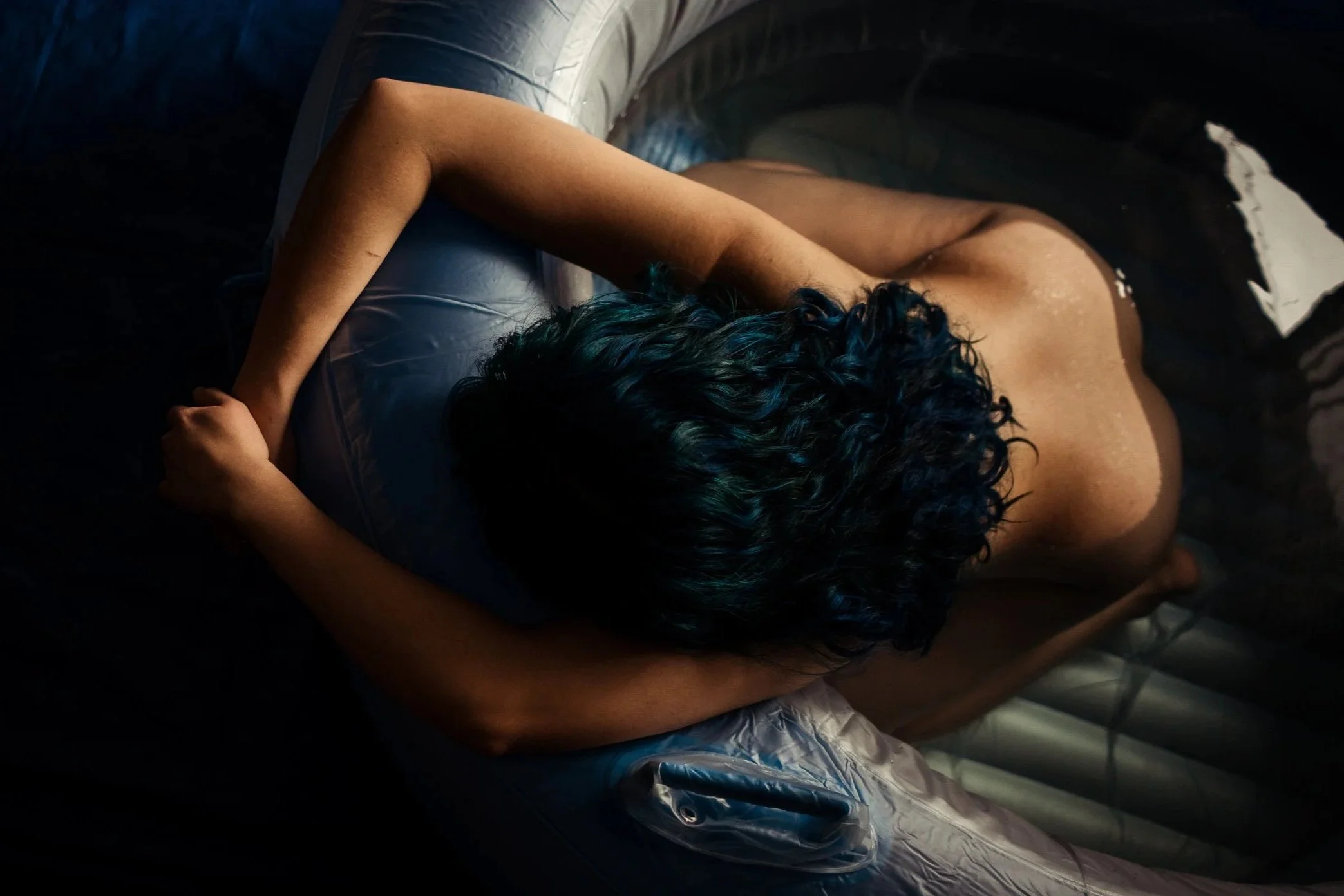 A person with curly dark hair lying face down in an inflatable pool, with their arms resting on the edge.