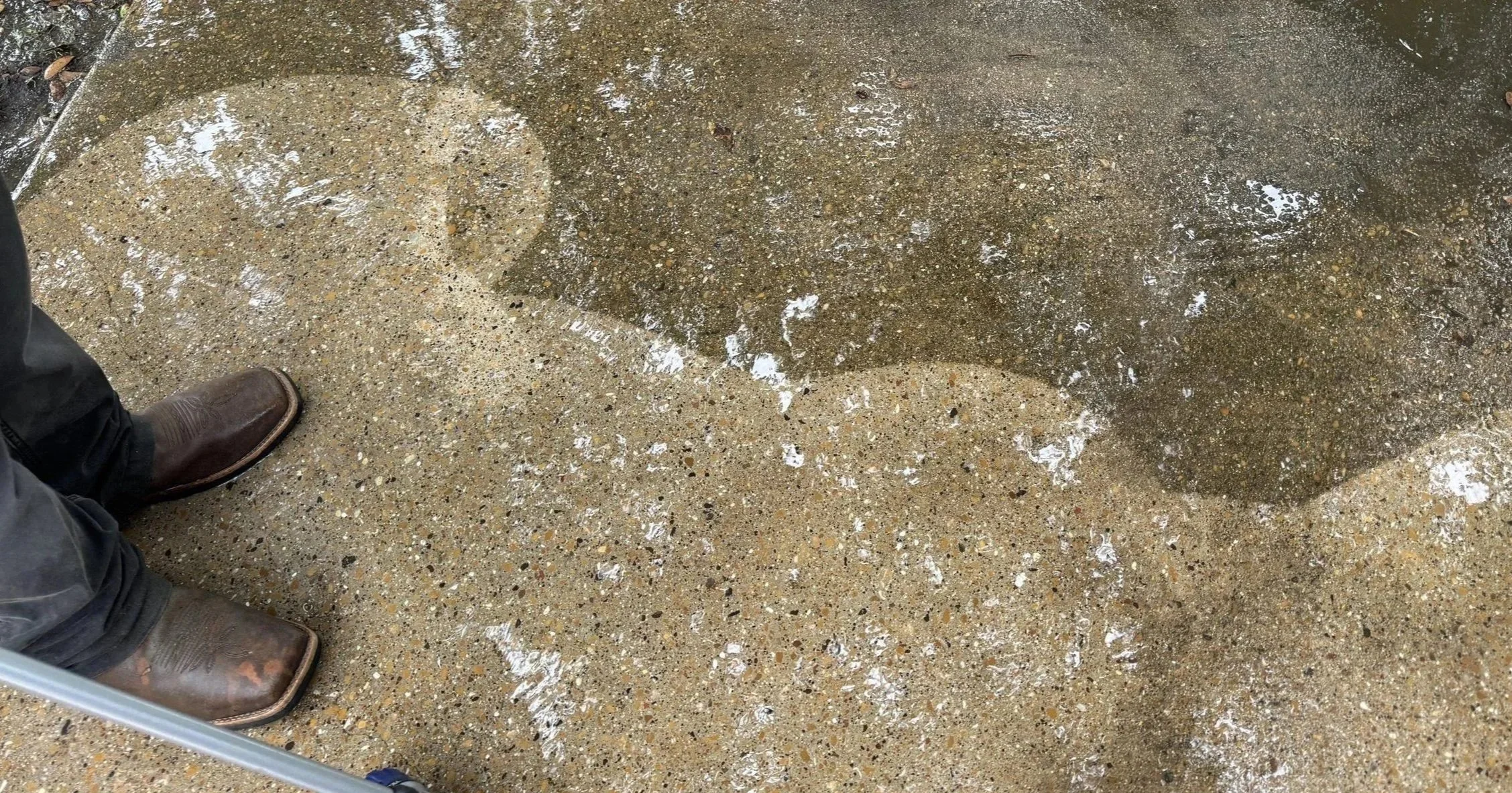 Spotlite technician pressure washing an exposed aggregate patio in Dallas, showing the clean surface emerging