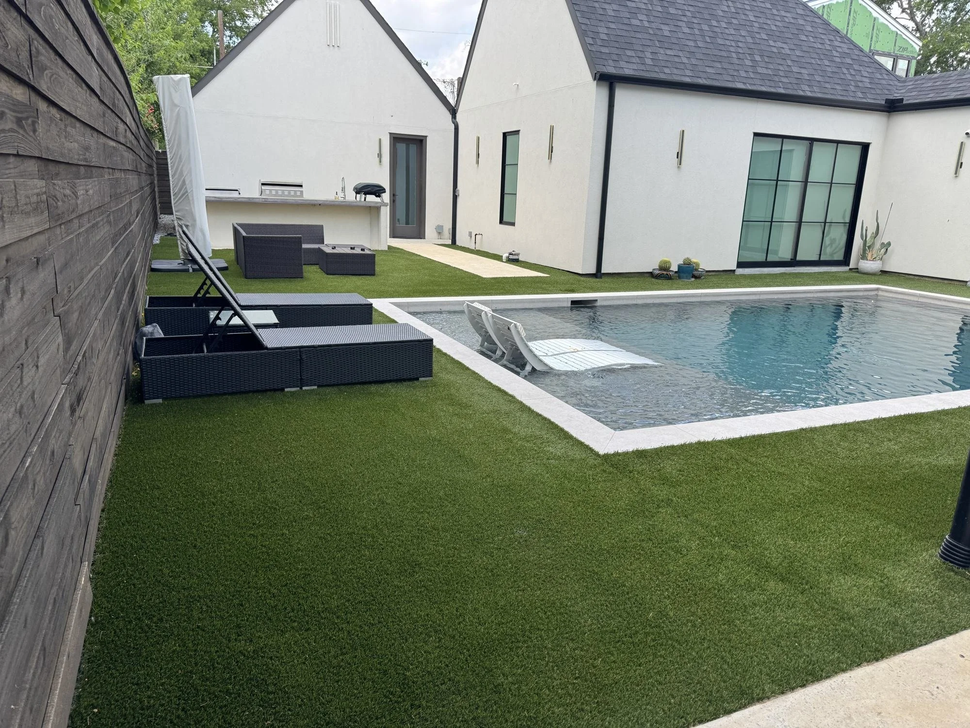 Artificial turf lawn surrounding a pool and outdoor kitchen at a Dallas home.