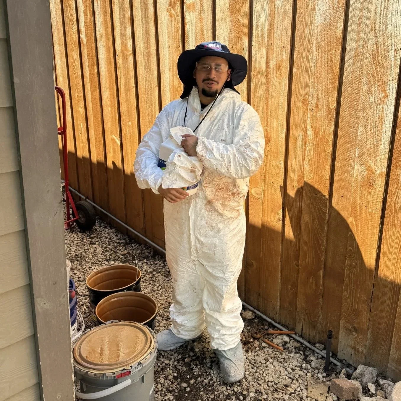 Spotlite technician in protective gear preparing stain for a freshly cleaned cedar fence, Dallas