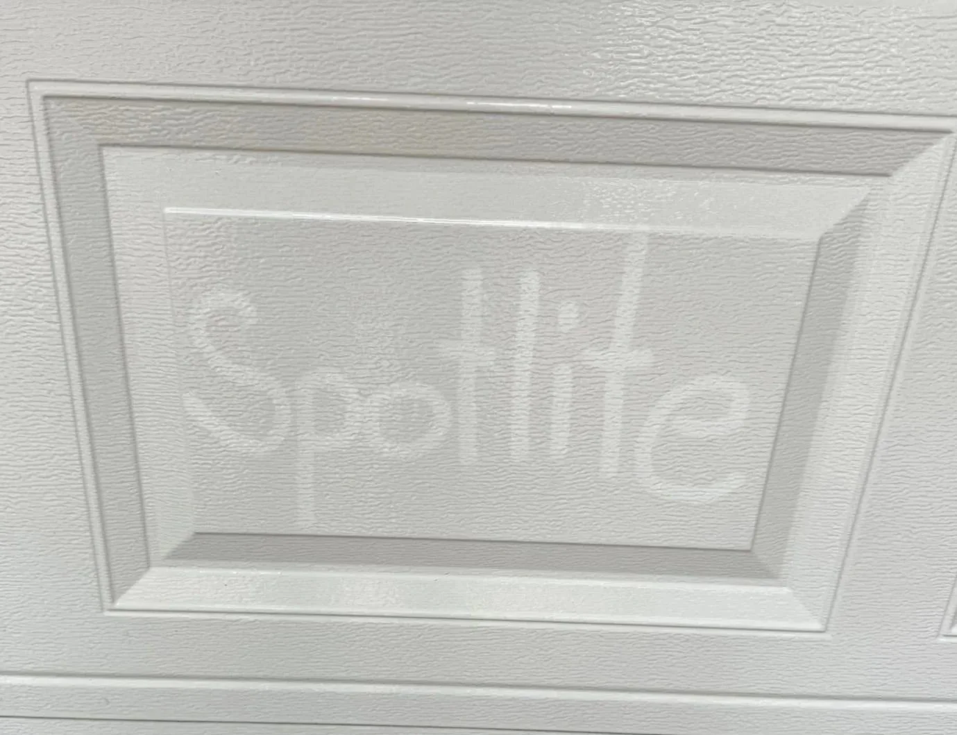 The Spotlite name finger-drawn through the grime on a white garage door — buildup you don't notice until it's gone