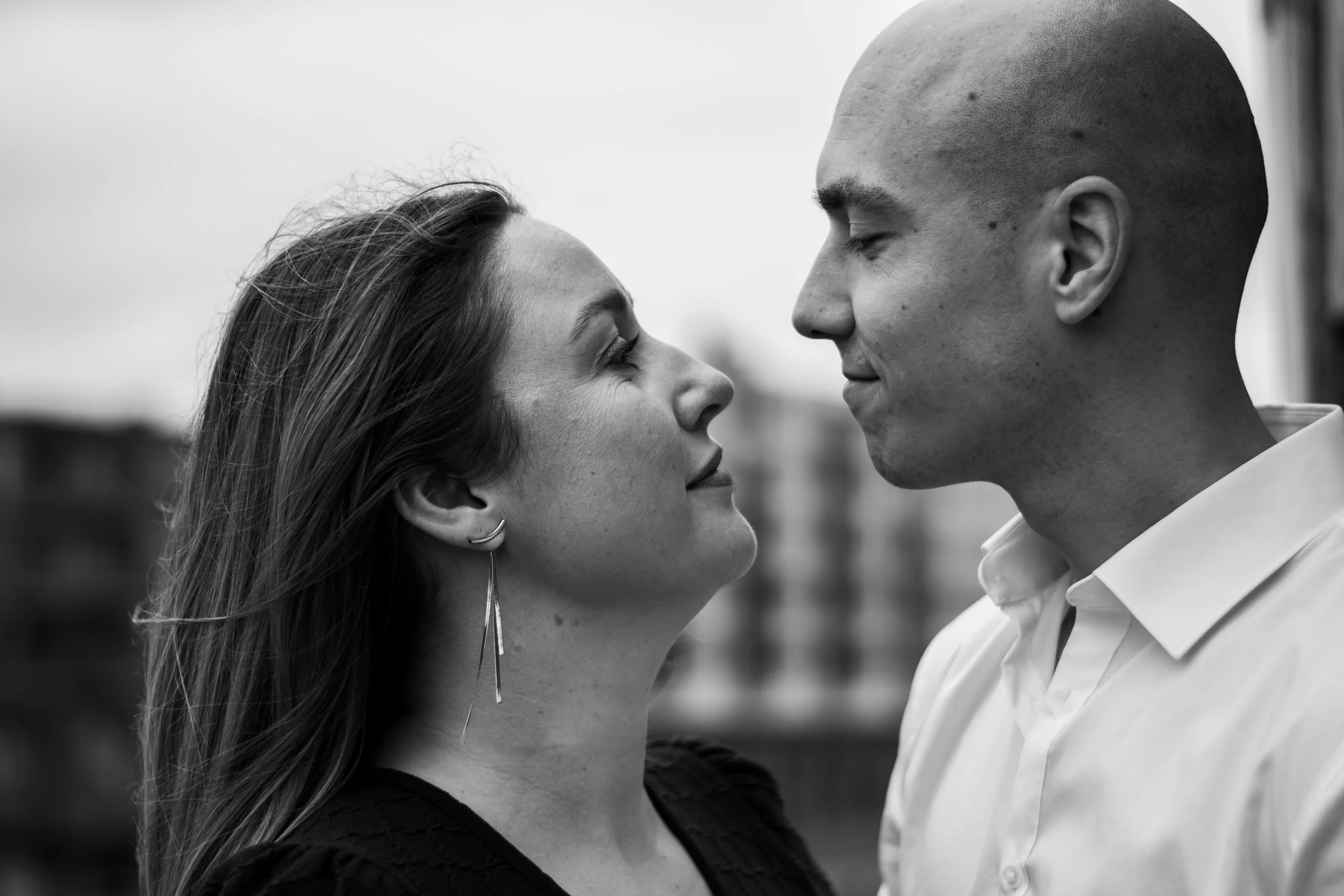 A black-and-white close-up of a woman and a man face to face, gazing into each other's eyes outdoors.