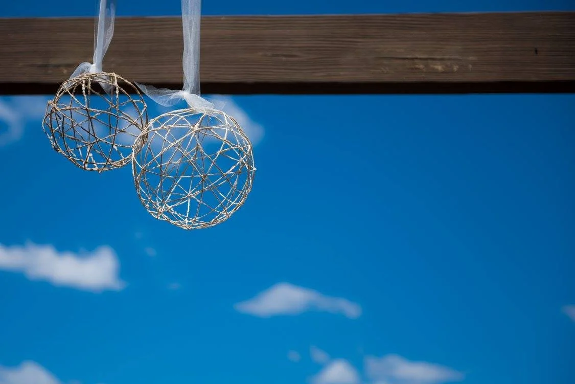 Two decorative spherical wicker balls hanging from a wooden beam against a blue sky with scattered clouds.
