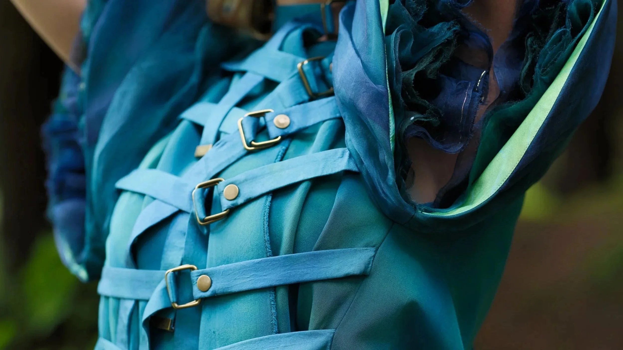Turquoise shibori-dyed sculptural garment with straps and hardware, referencing restraint and release in the Damage/Repair series.