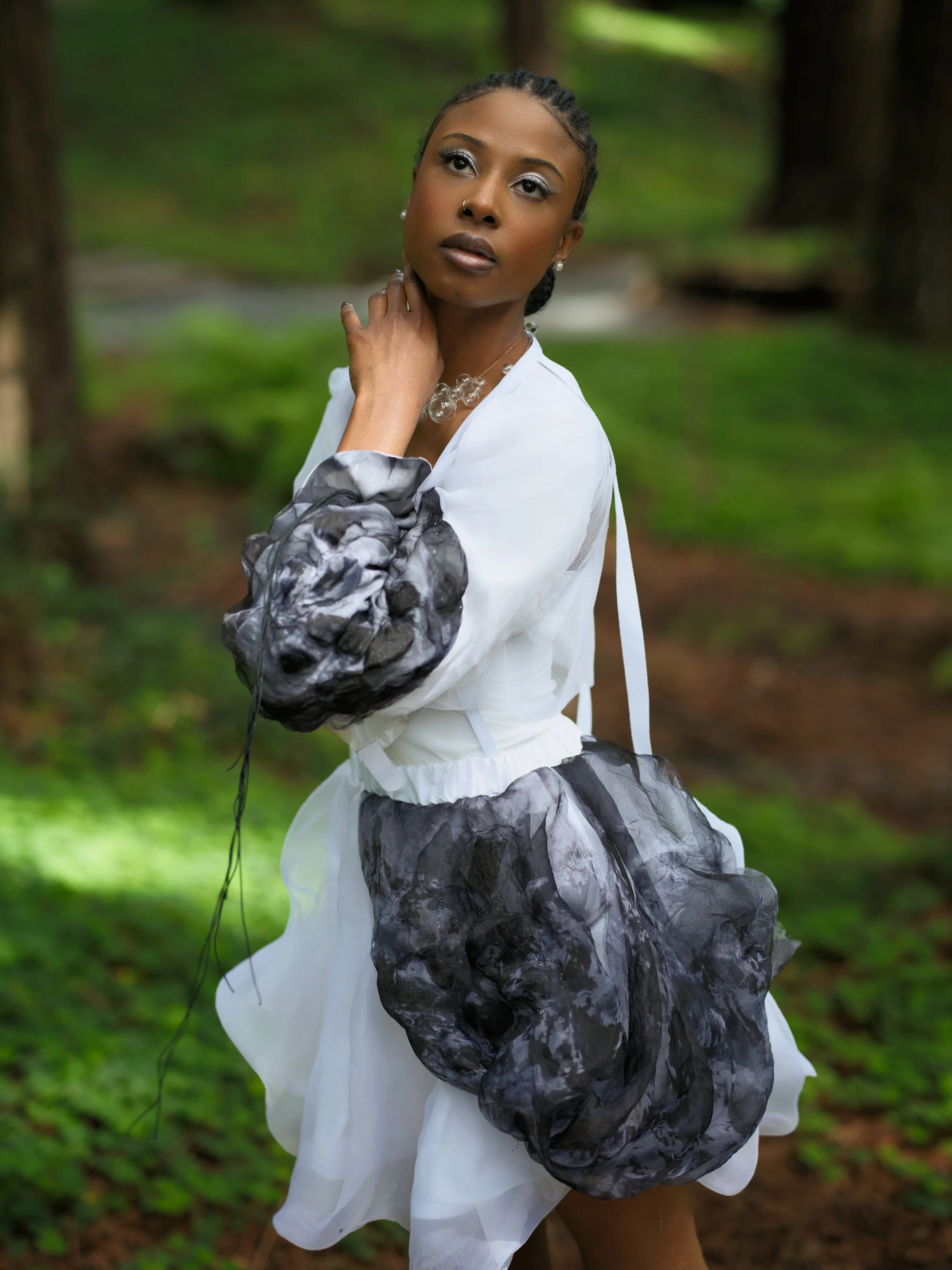 Model wearing a sculptural art-to-wear piece in a forest setting, connecting body, garment, and landscape within the Damage/Repair series.