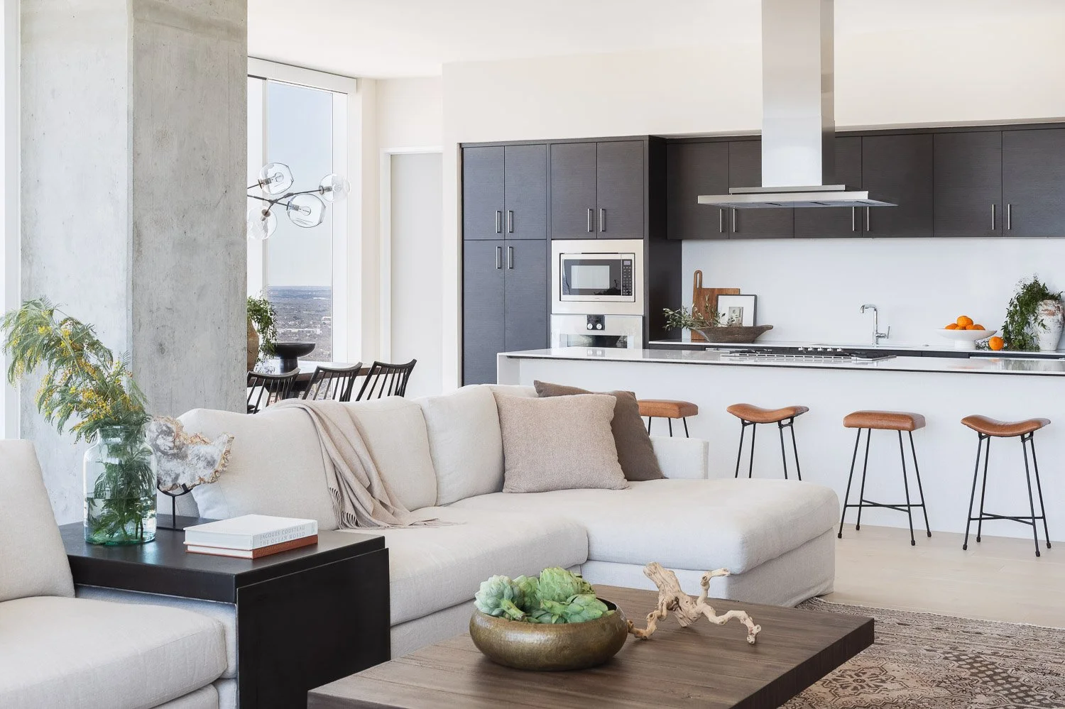 Modern open-concept living room and kitchen with a light-colored sofa, dark kitchen cabinets, and barstools.