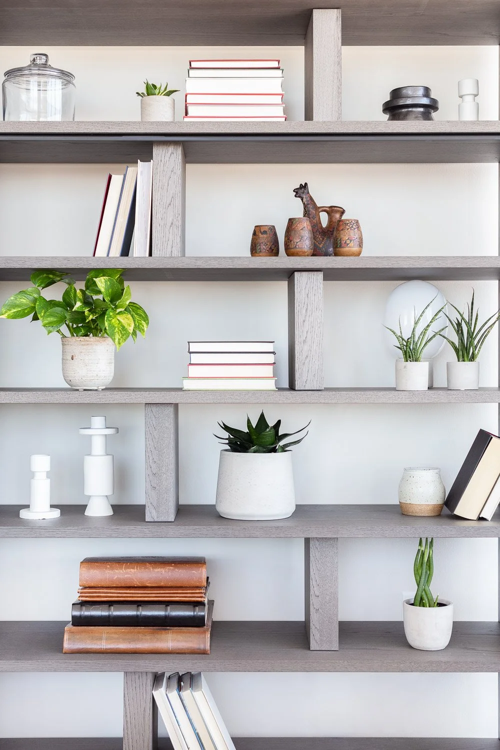 A modern grey wooden bookshelf with plants, books, and decorative objects arranged on its shelves.