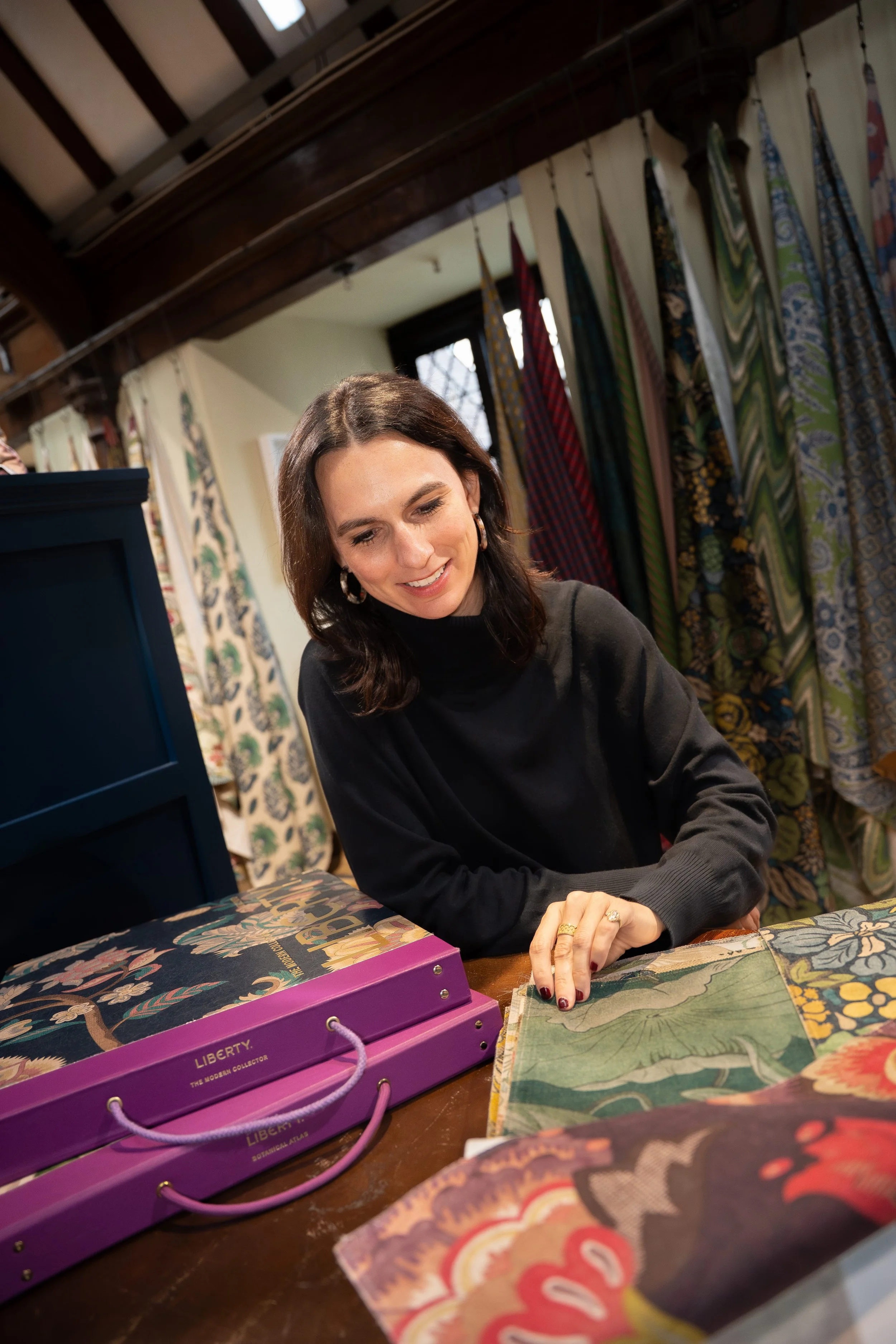 Woman shopping for fabric in a store with colorful fabrics hanging behind her.