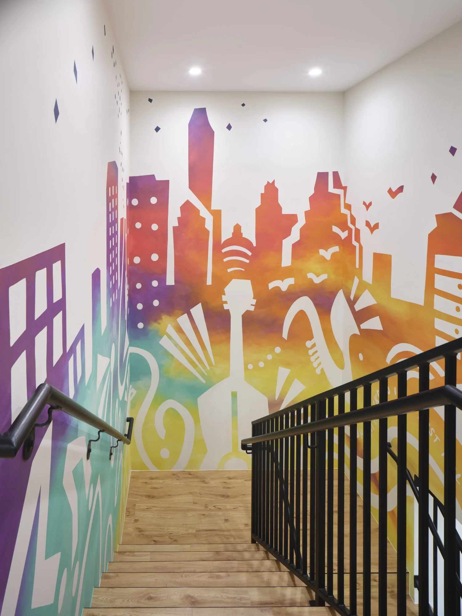 Colorful mural of city skyline and abstract shapes on a stairwell wall.
