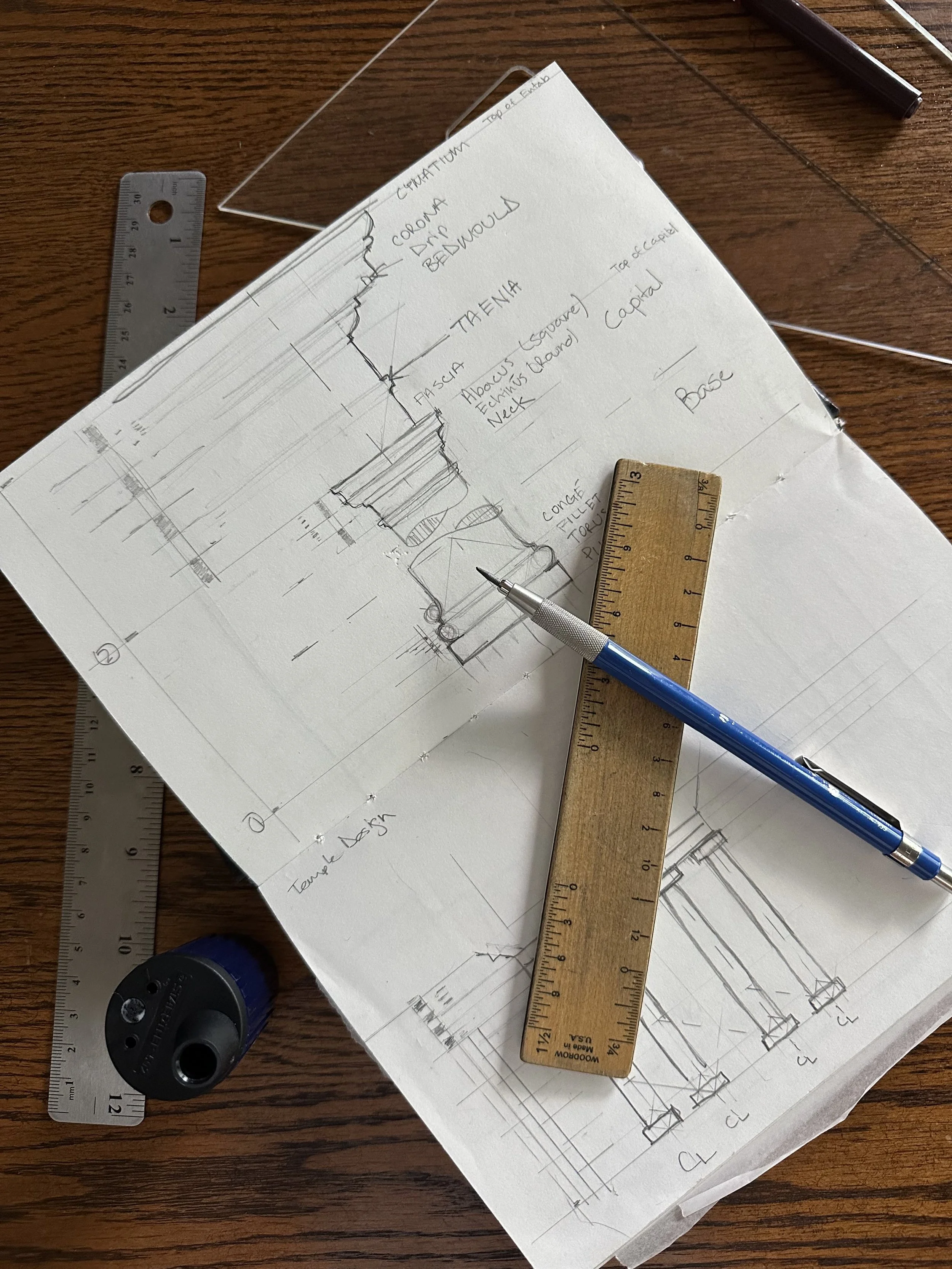 Sketches and notes for architectural or furniture design on paper with tools like a ruler, pen, and a small weight flat on the table.