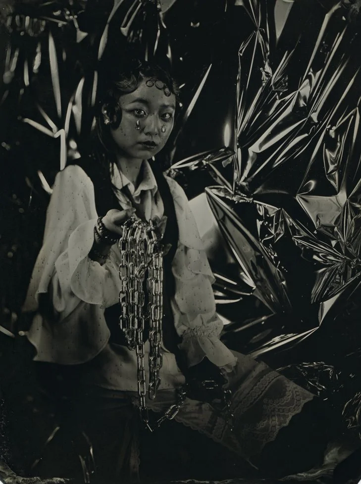 a tintype portrait of a young Korean person with a dynamic background holding chains