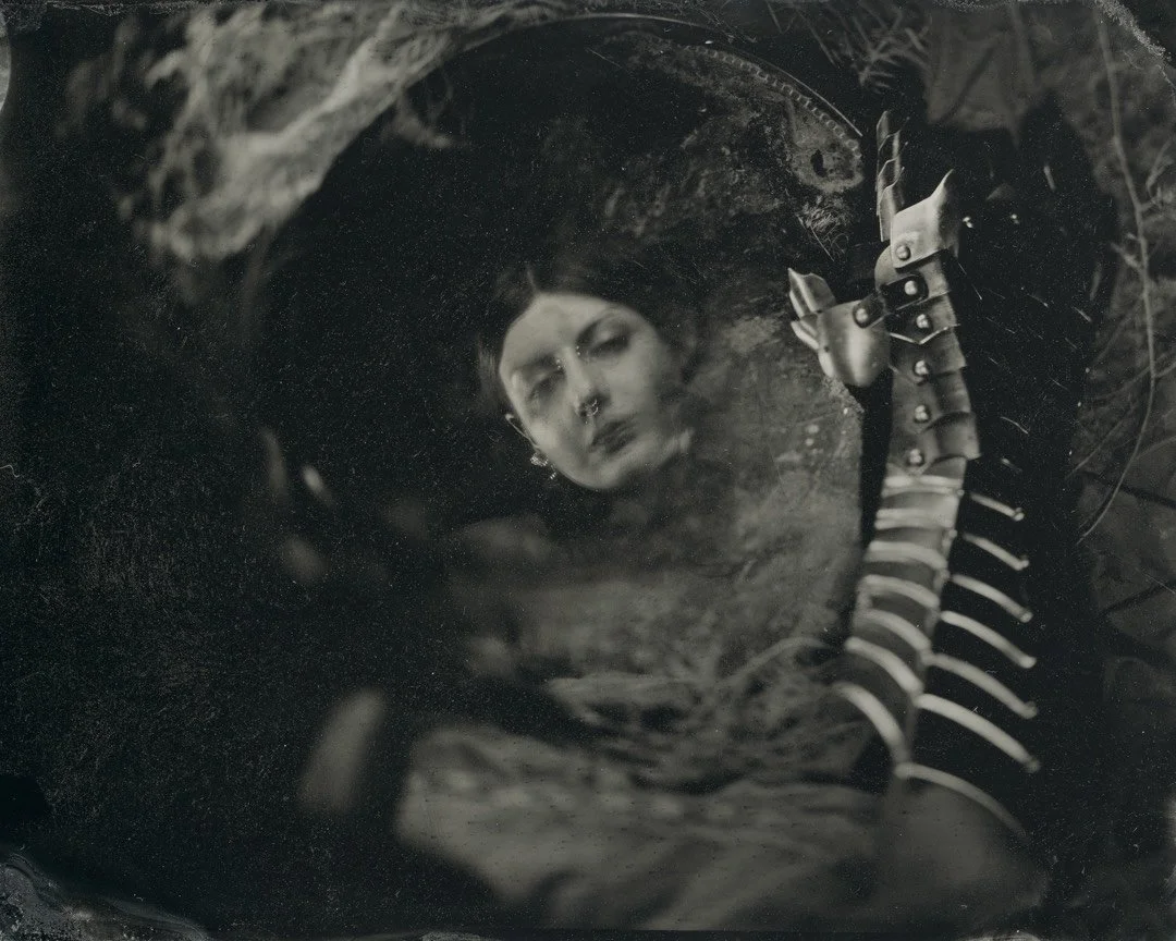 a slightly strange tintype portrait featuring the reflection of a young woman in a mirror being held by a metal armored hand