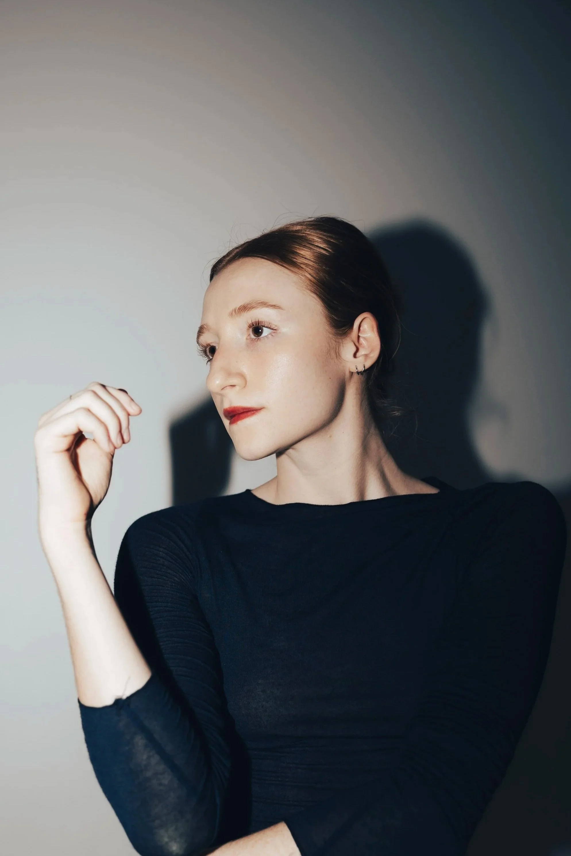 Portrait of a young woman with short, wavy auburn hair, wearing a white scarf with purple polka dots around her neck, standing against a plain light background.