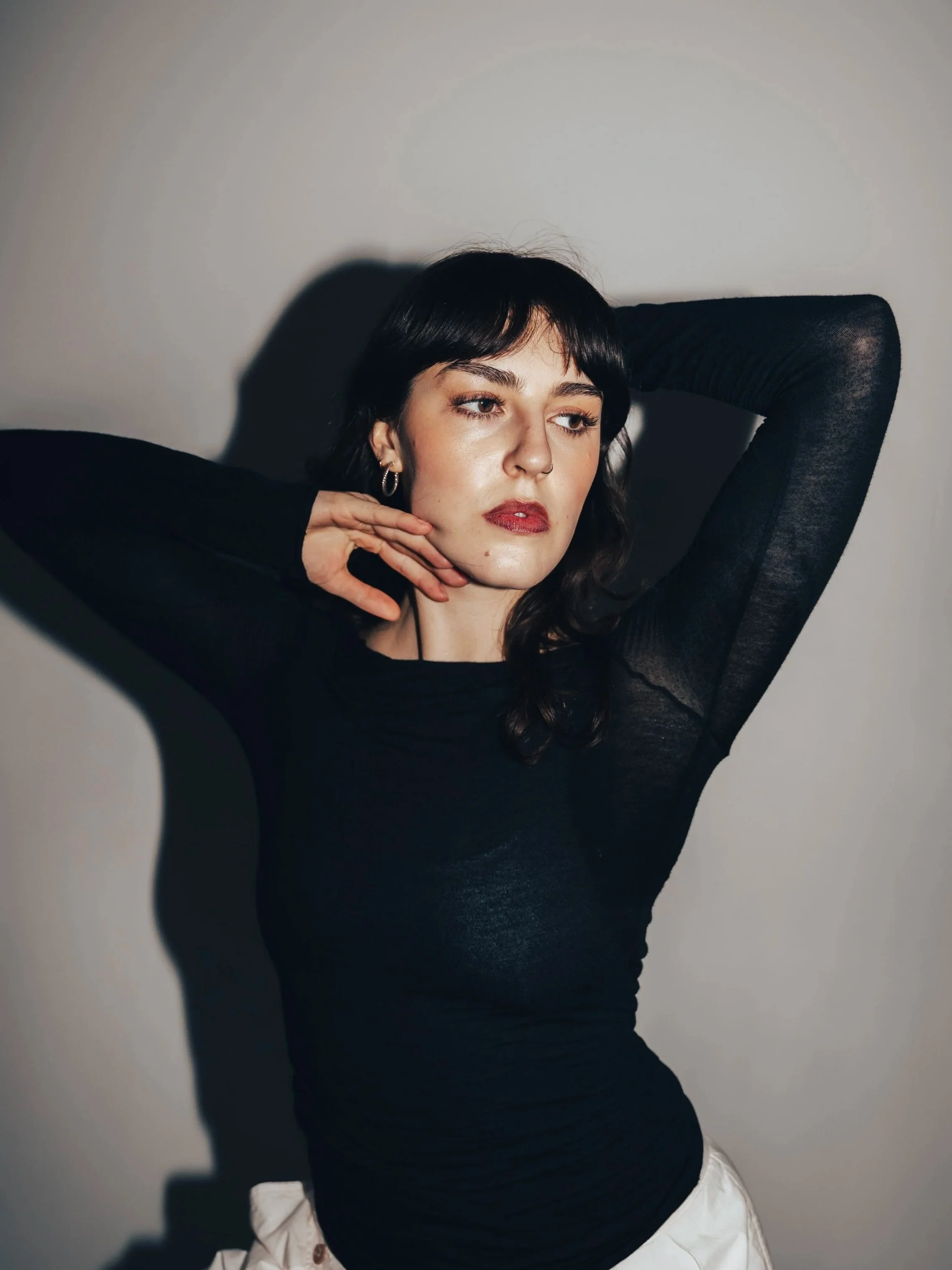 A woman with shoulder-length dark brown hair standing in front of white curtains.