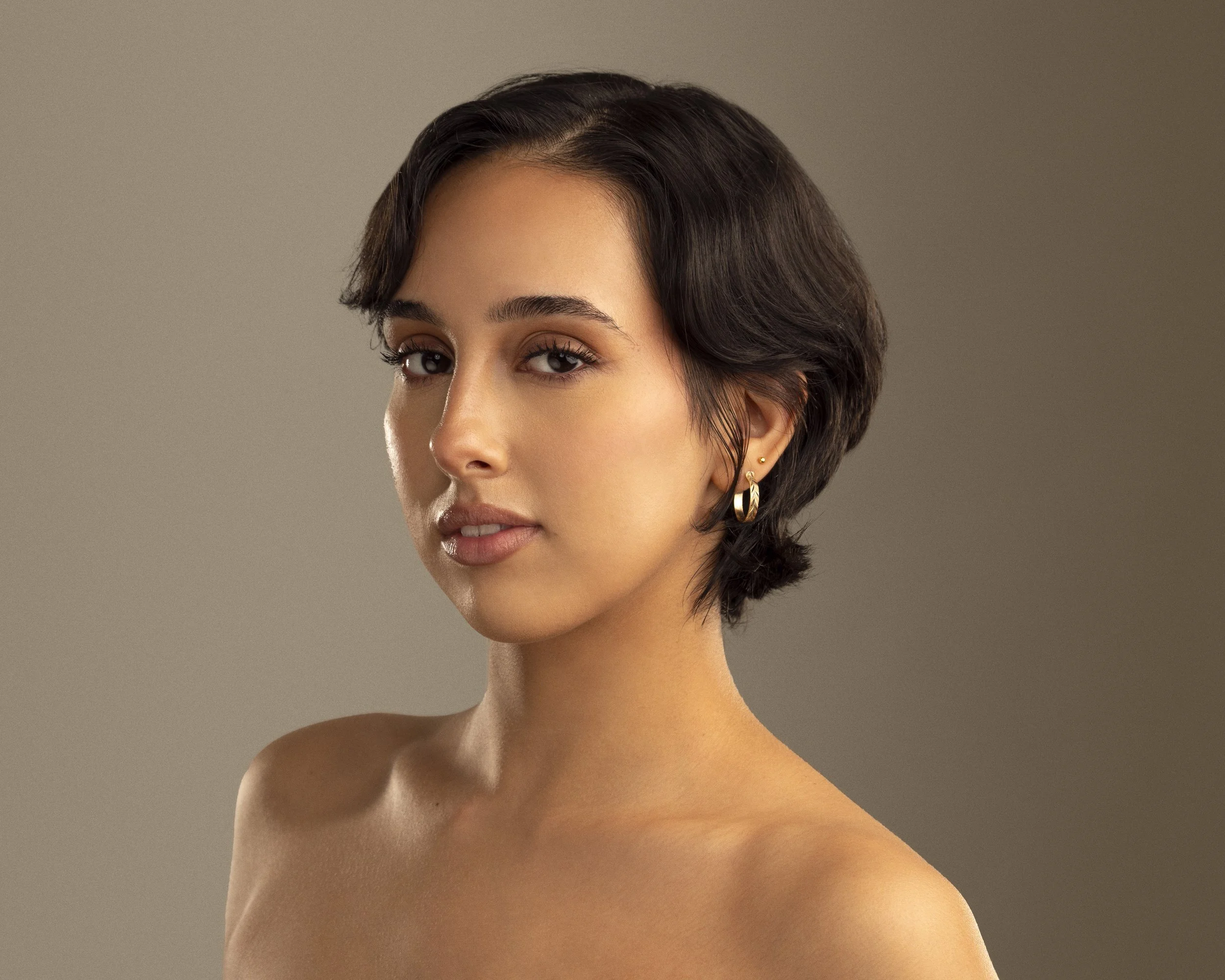 A portrait of a young woman with short dark hair, wearing gold hoop earrings, looking at the camera with a neutral expression.