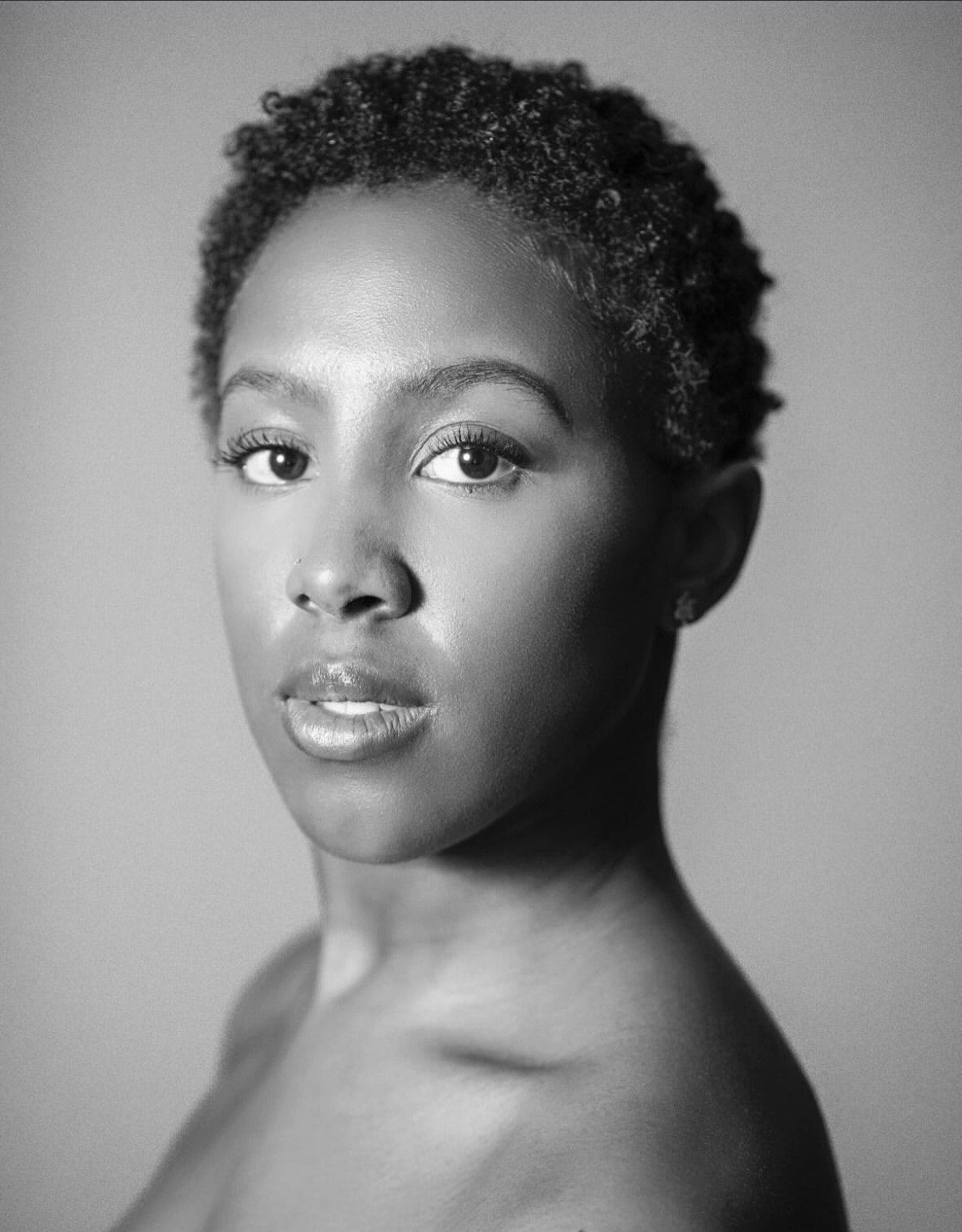 Black and white portrait of a woman with short, natural hair, looking directly at the camera with a neutral expression.