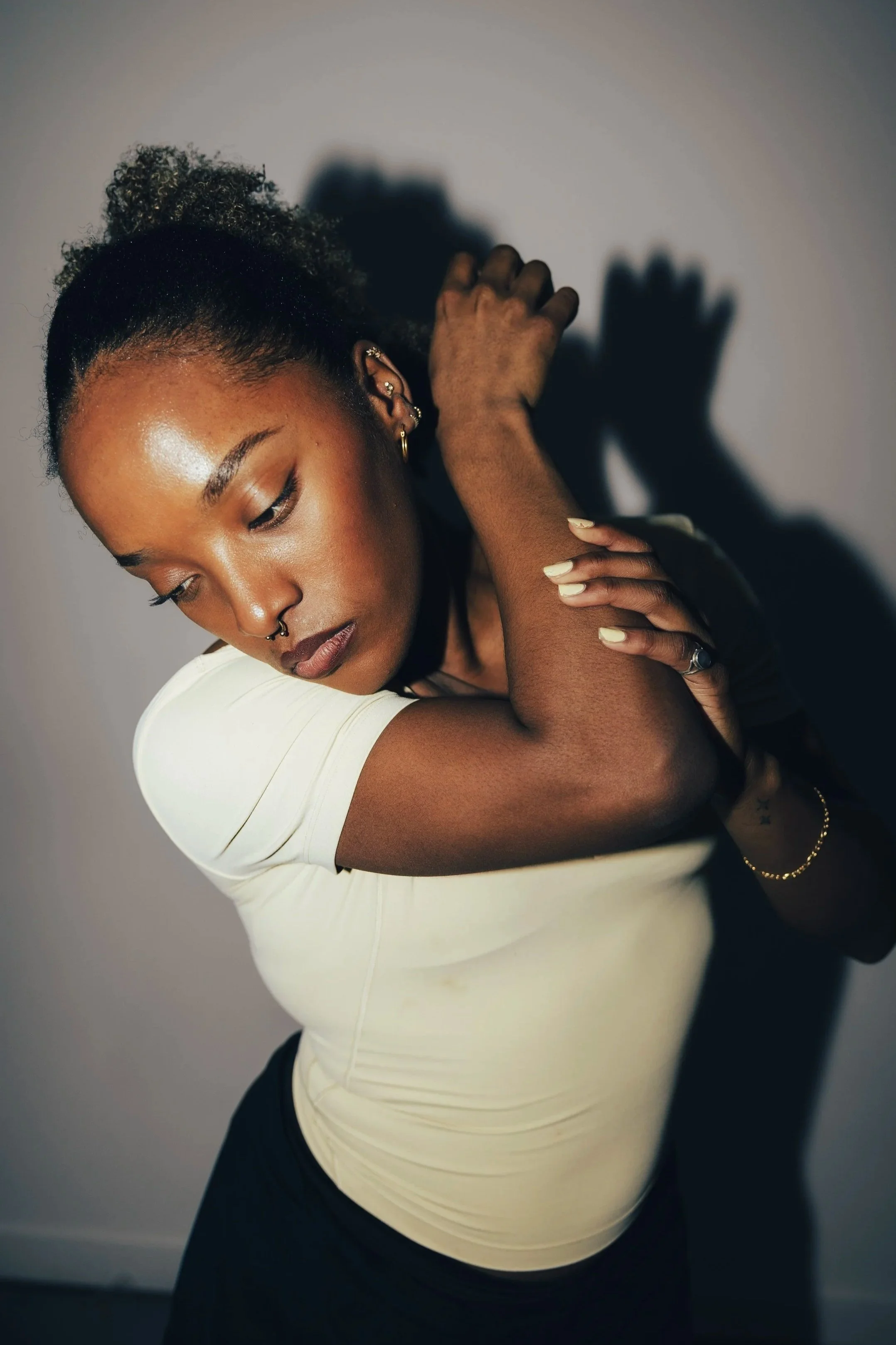 Black and white portrait of a woman with curly hair, wearing hoop earrings, and a septum piercing, looking directly at the camera.