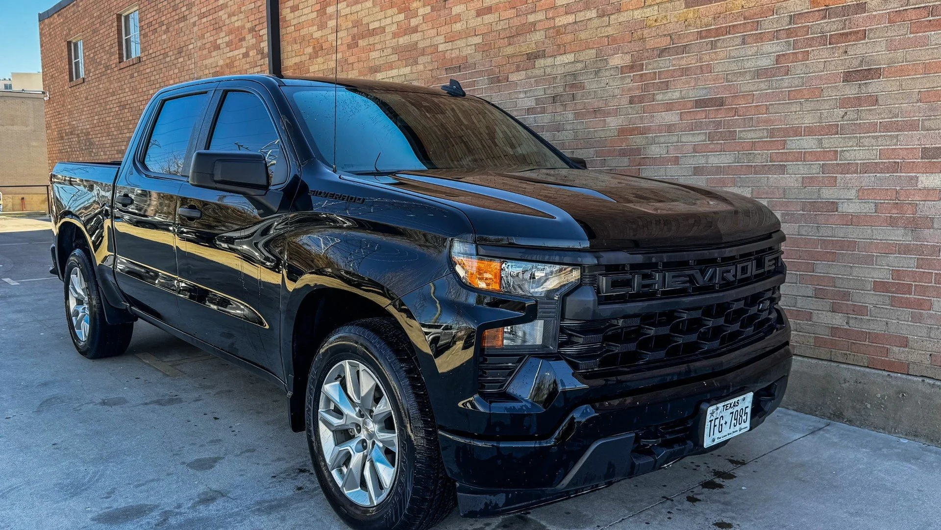 Black Chevrolet Silverado pickup truck parked near a brick wall in an urban area.