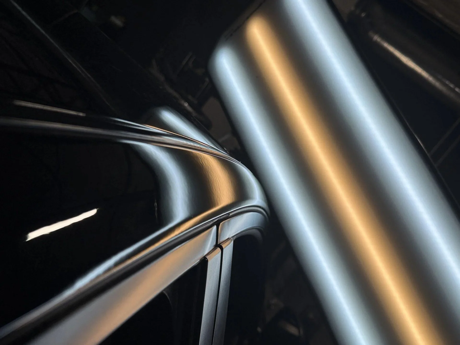 Close-up of shiny, metallic kitchen appliances, possibly an oven and a range hood, with reflections and black background.
