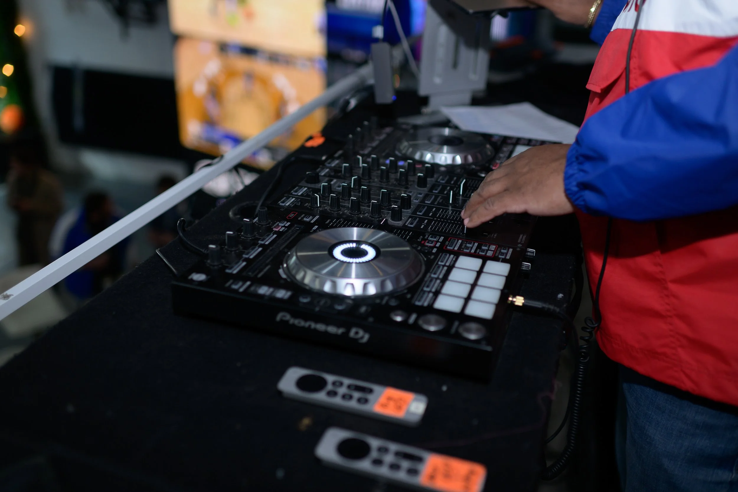 A DJ in a red and blue jacket mixing music on a Pioneer DJ controller at an event or party.