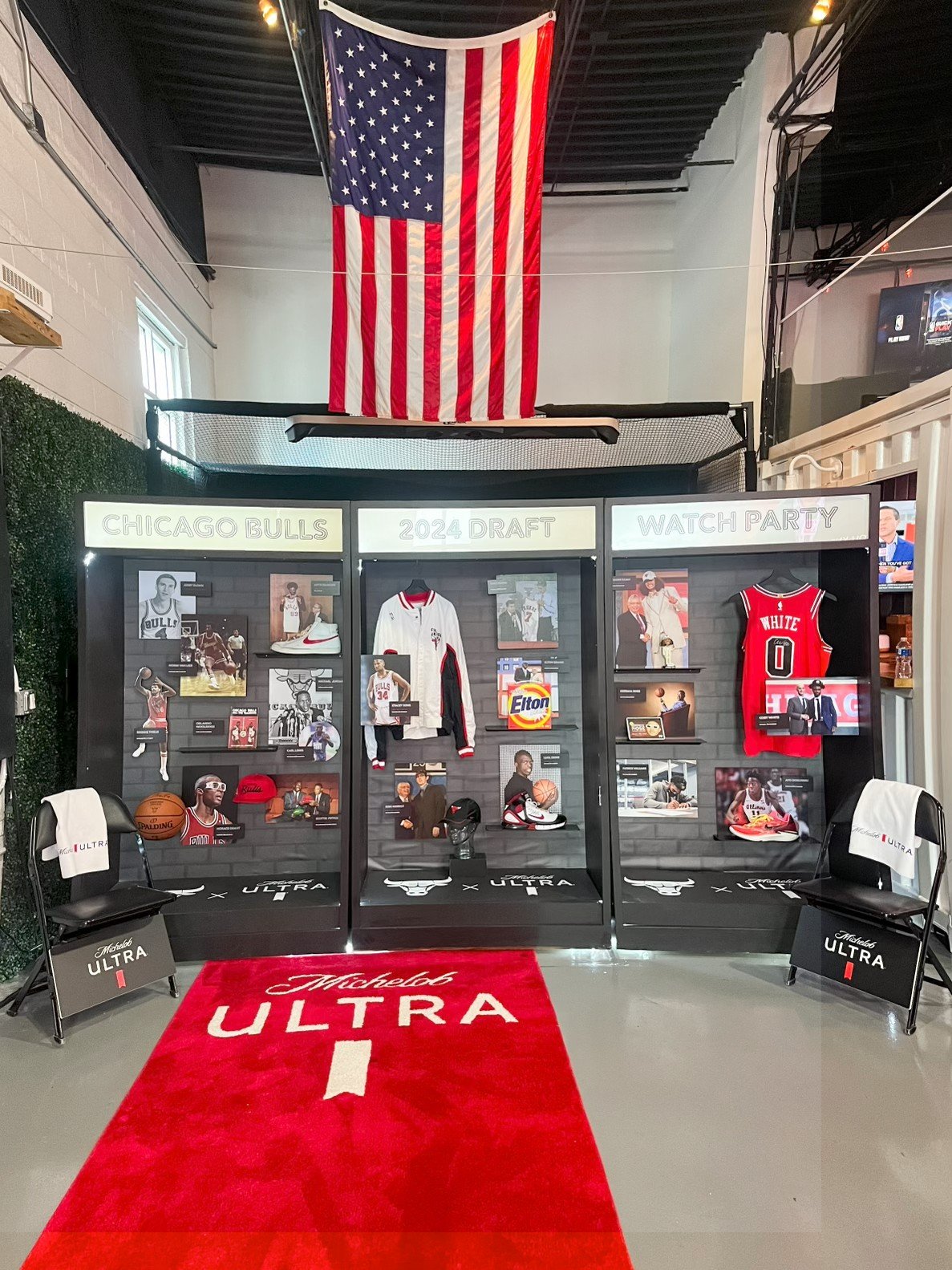 Display featuring Chicago Bulls memorabilia, including jerseys, photos, and basketball gear, with a Chicago Bulls red carpet in the foreground and an American flag hanging above.
