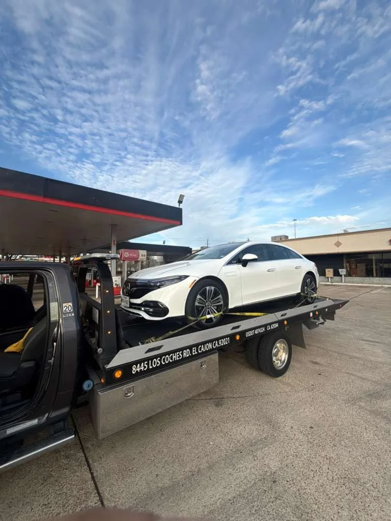 White sedan car on a flatbed tow truck in a parking lot.