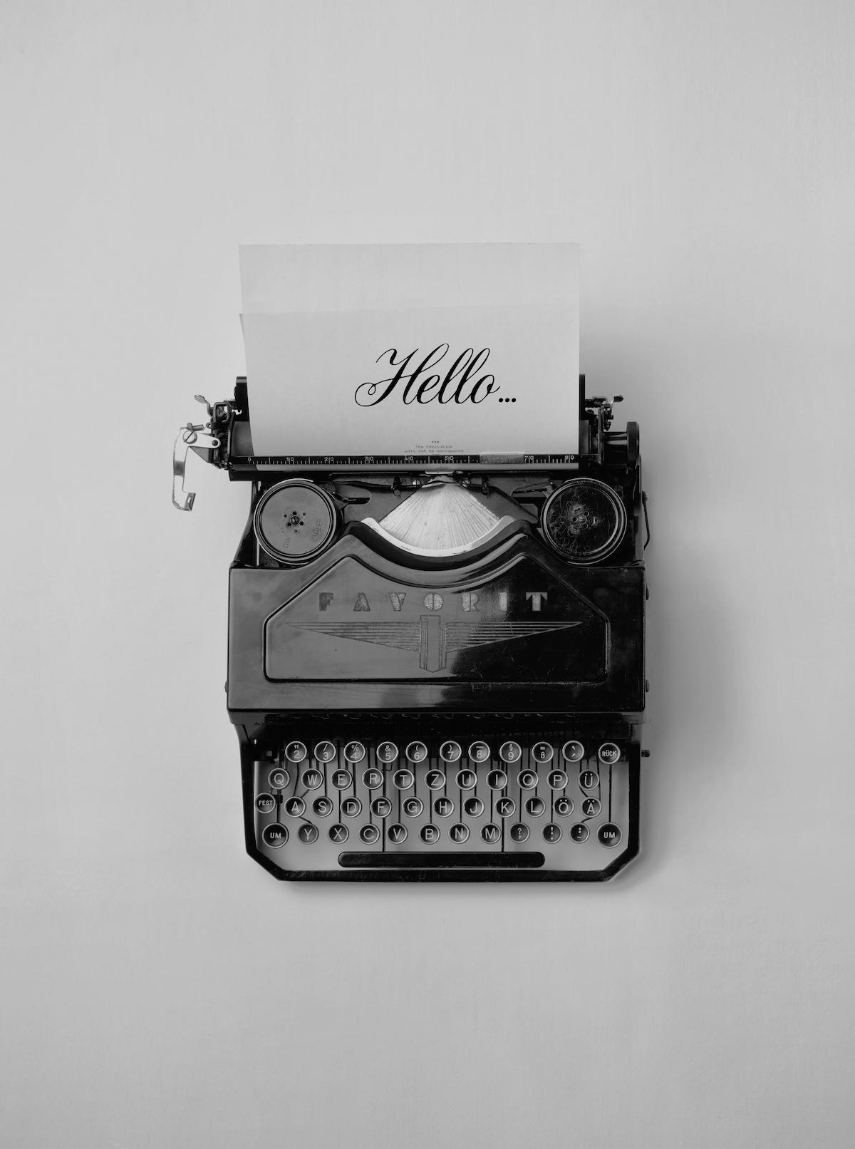 Black and white photo of a vintage typewriter with a paper that says "Hello..." on a plain white background.