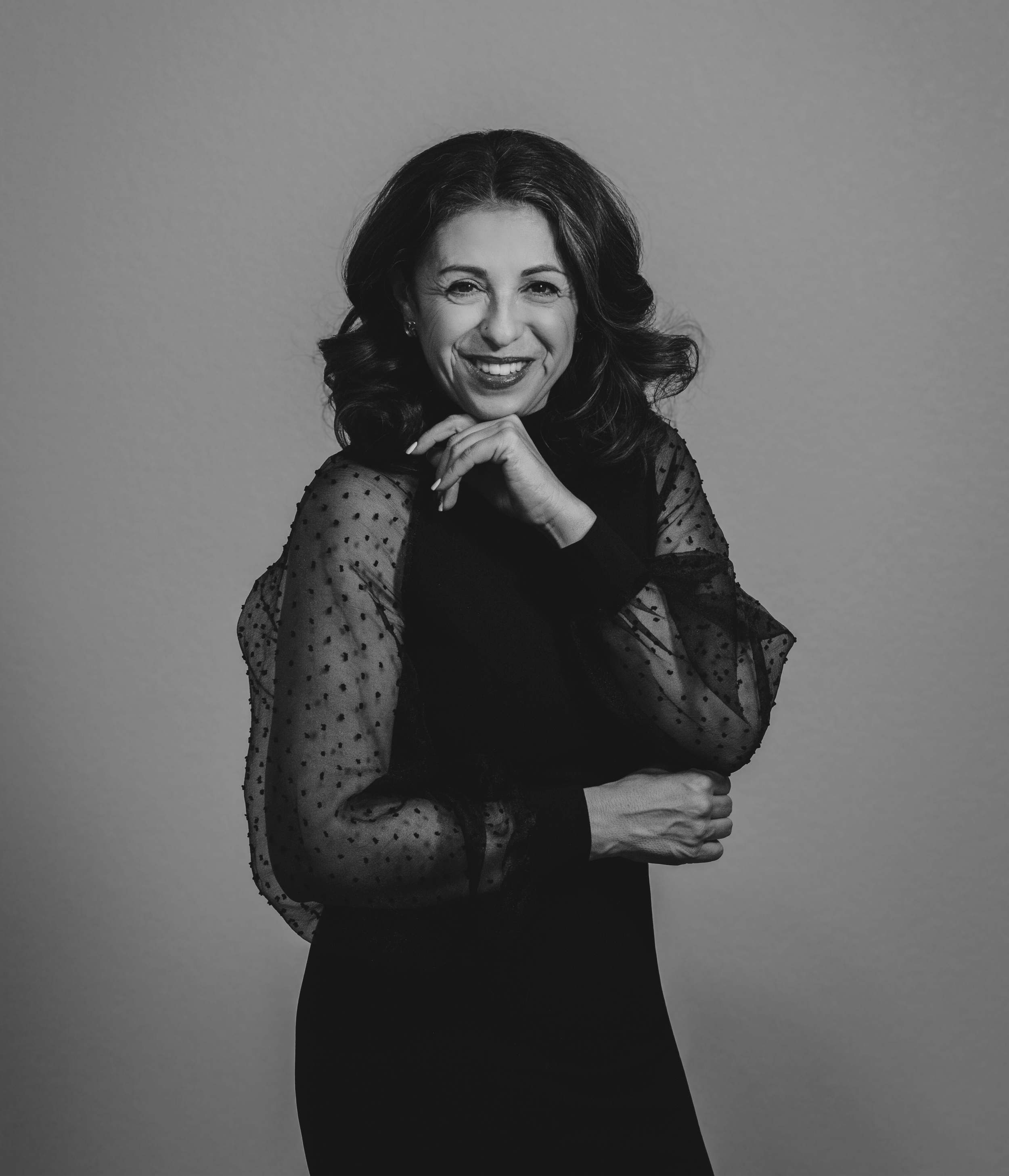 Black and white portrait of a smiling woman with wavy hair, wearing a dress with sheer polka-dot sleeves
