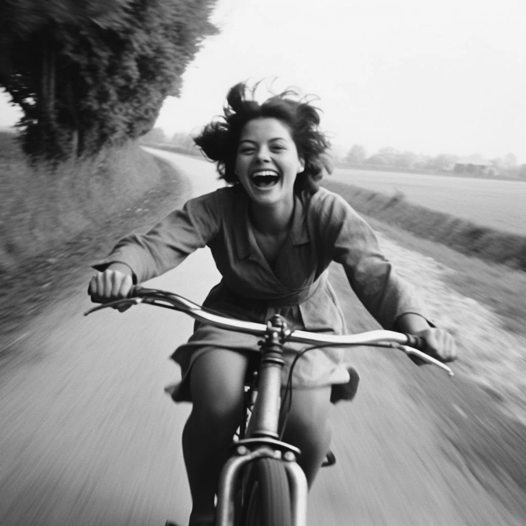 A woman riding a bicycle on a rural road, smiling and enjoying the ride, with trees and open fields in the background.