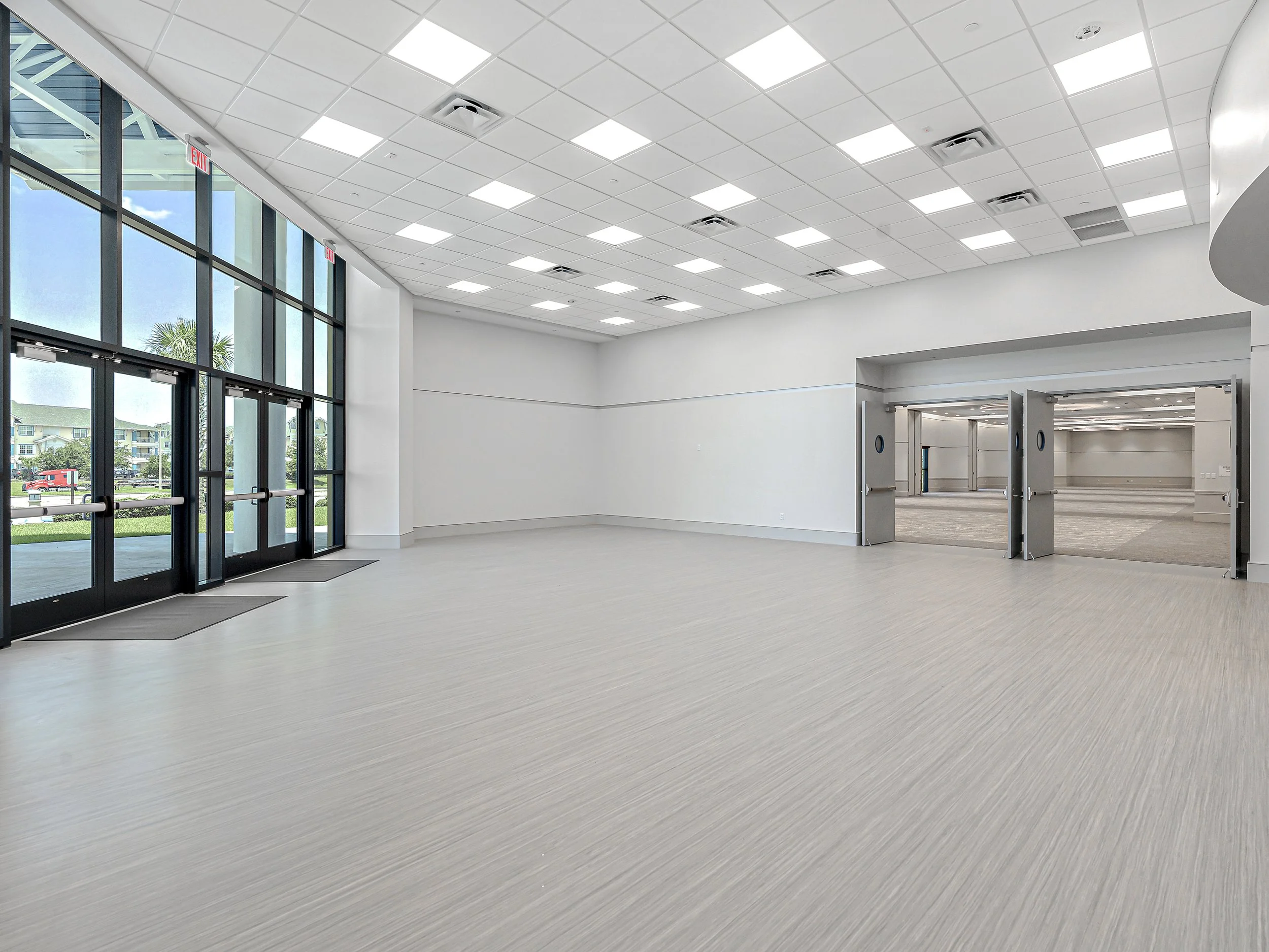 Empty spacious modern conference or event hall with large glass entrance doors, white walls, and a ceiling with square lights.