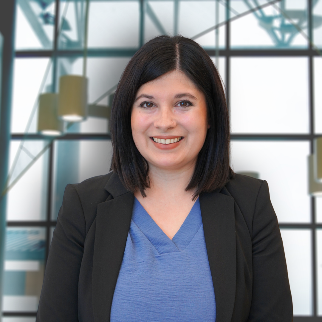 Professional woman with black hair smiling in an office with glass windows and geometric architecture.
