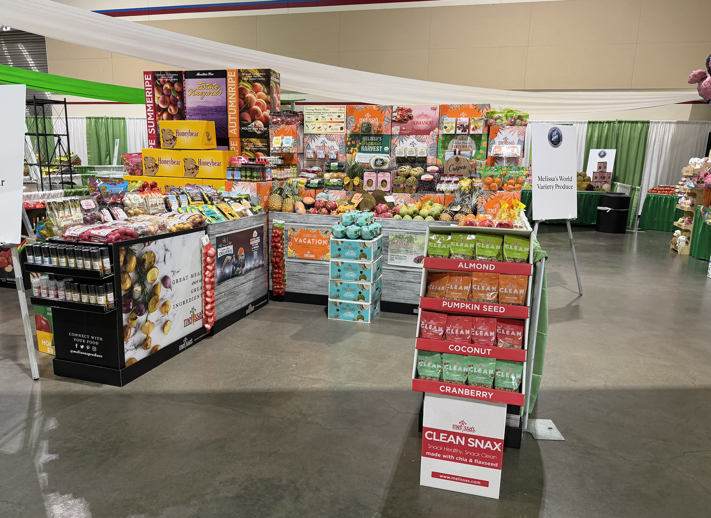 Display of fresh fruits and snacks at a vendor booth in a convention center, including apples, pineapples, and packaged snack foods.