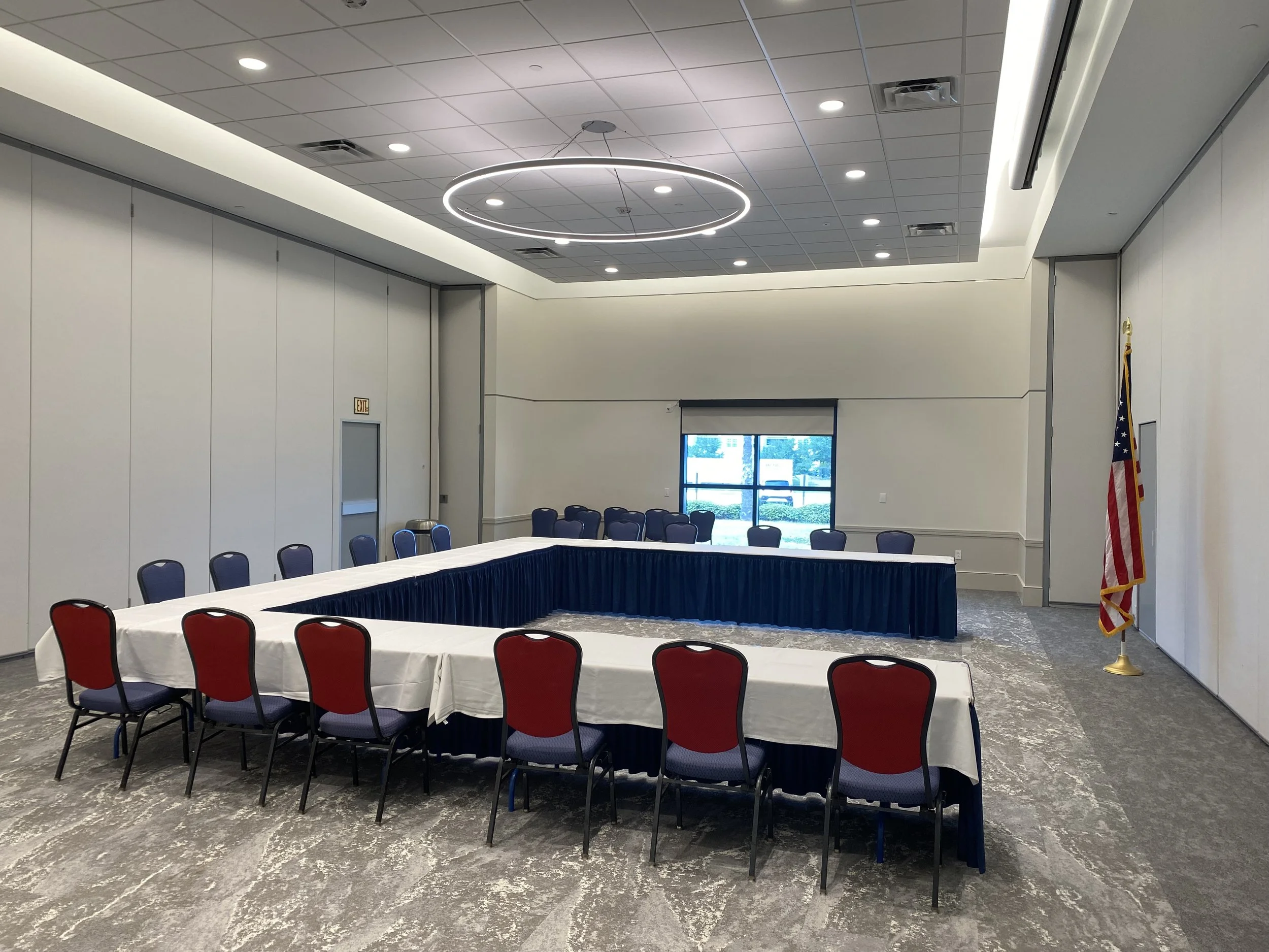 Empty conference room with U-shaped table setup, blue chairs, American flag, and large windows