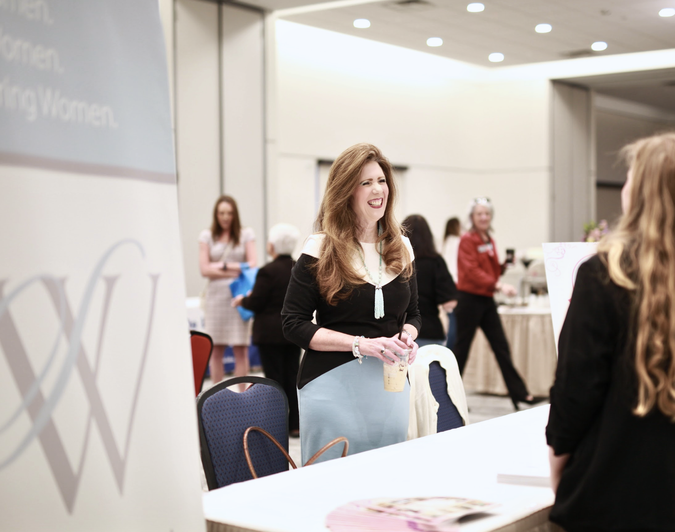 Women engaging in conversation at a conference or workshop, with a woman smiling and holding a coffee cup in focus.