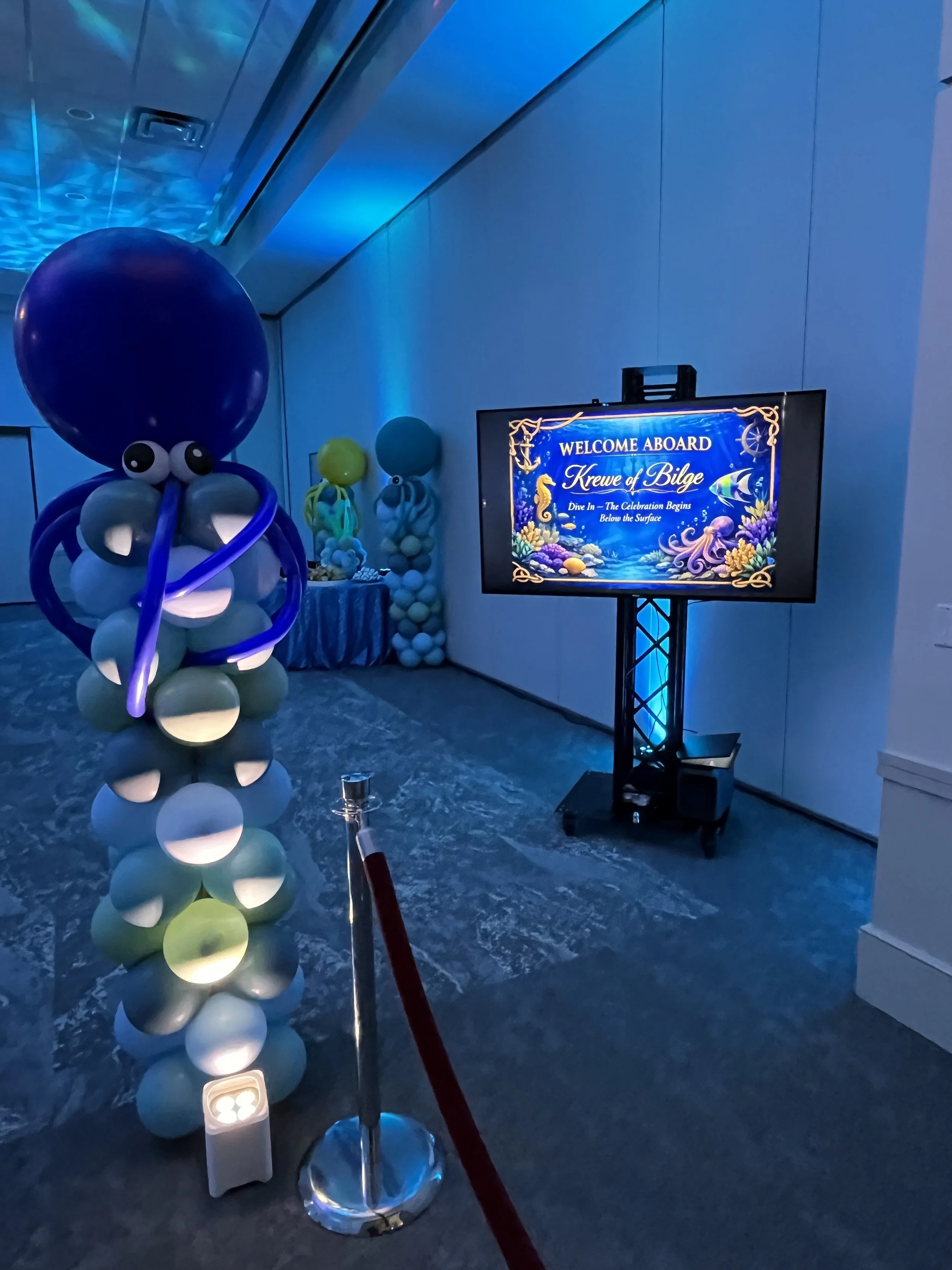 Decorations with balloon octopus and an underwater themed welcome sign on a television screen at a drive-in event.