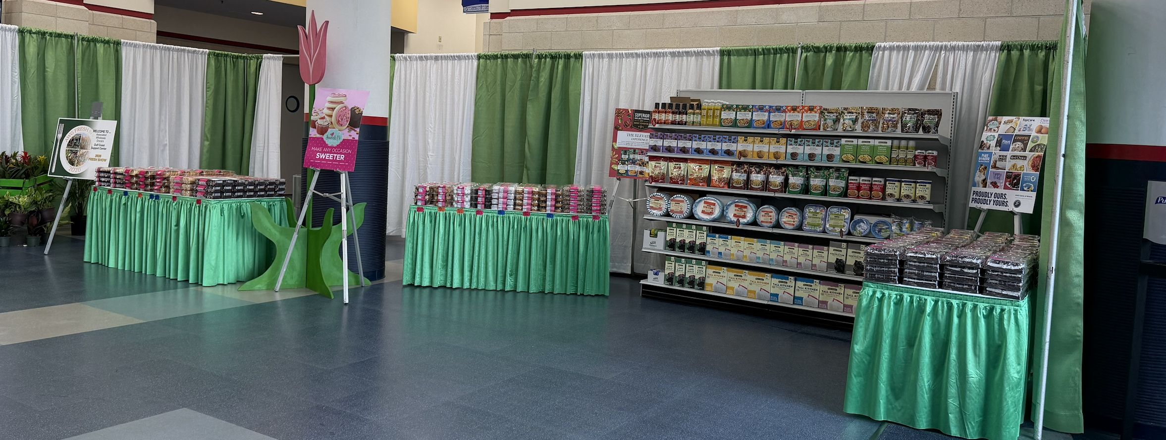 Display of packaged food products on shelves and tables with green and white curtains in the background at an indoor event.