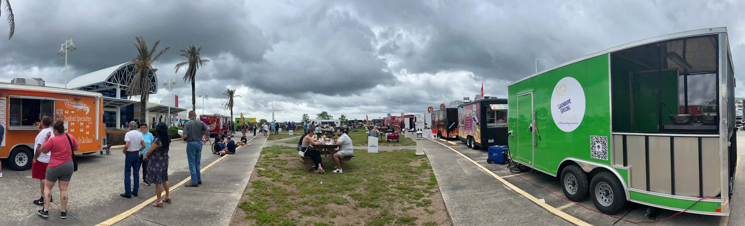 Food trucks and people gathered outdoors near a market with dark, cloudy sky overhead.