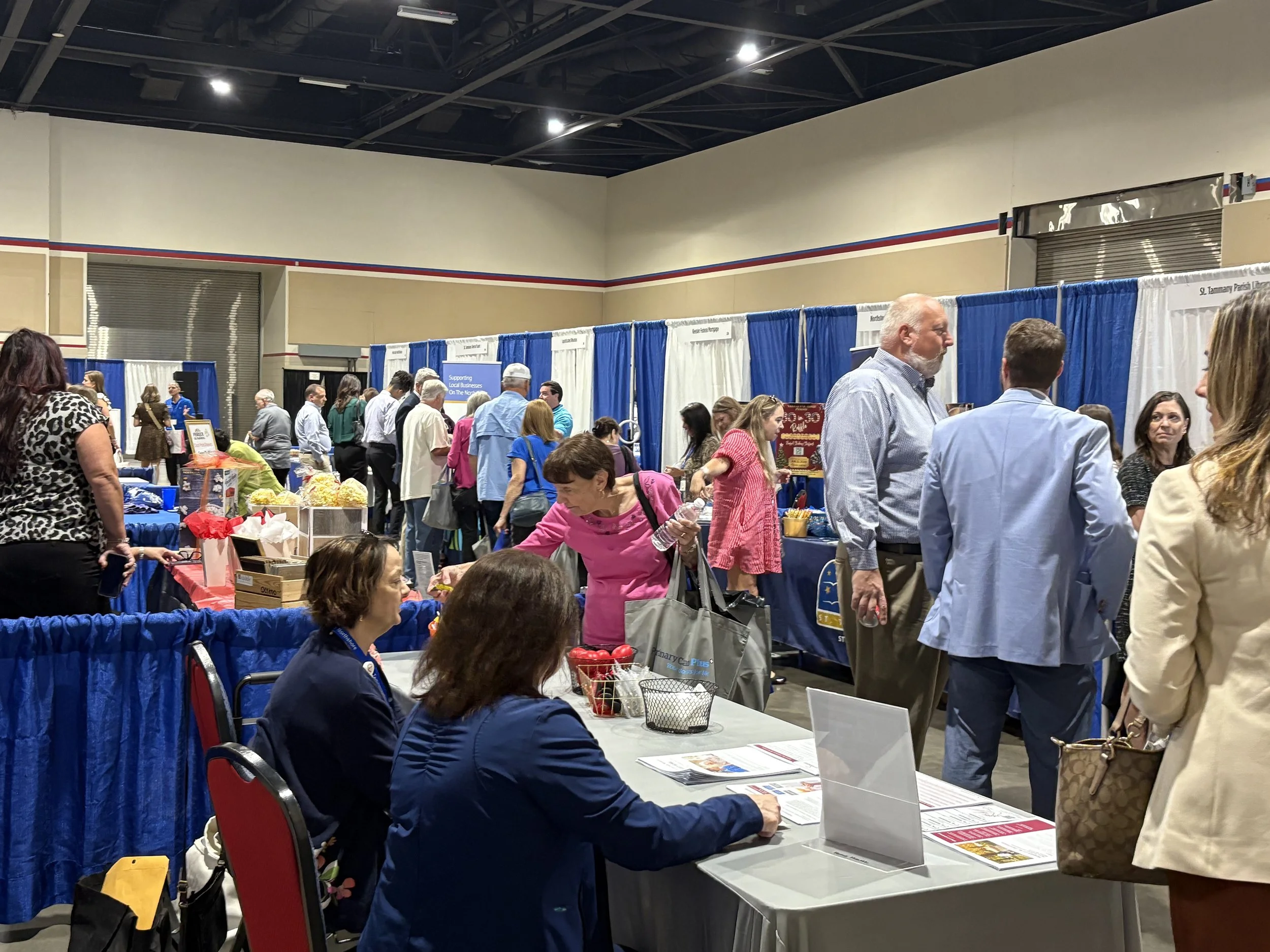 People attending a busy indoor expo or trade show with various booths and tables.